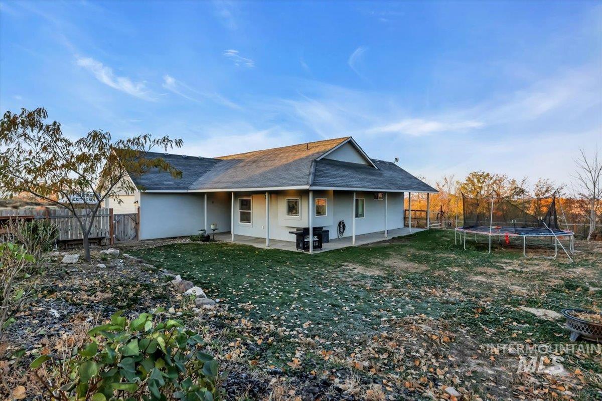 Rear view of house with a trampoline, a patio, roof with shingles, and a fenced backyard