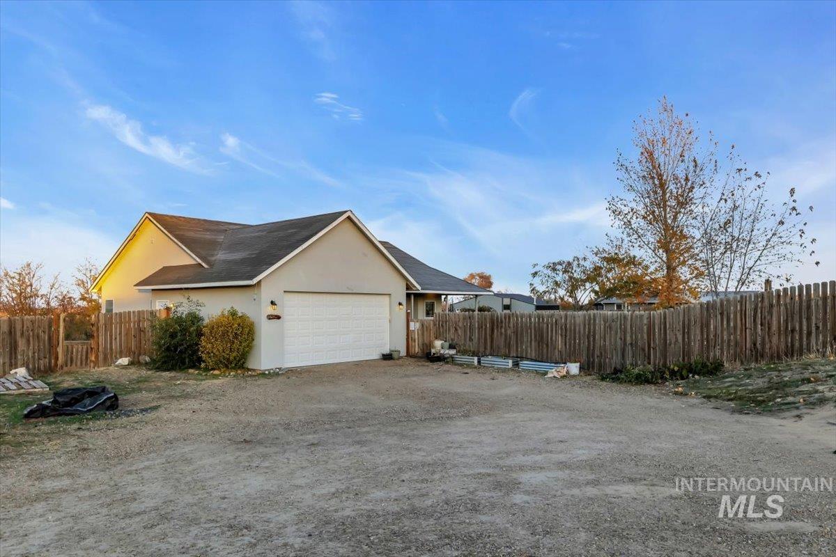View of property exterior with stucco siding, dirt driveway, and a shingled roof