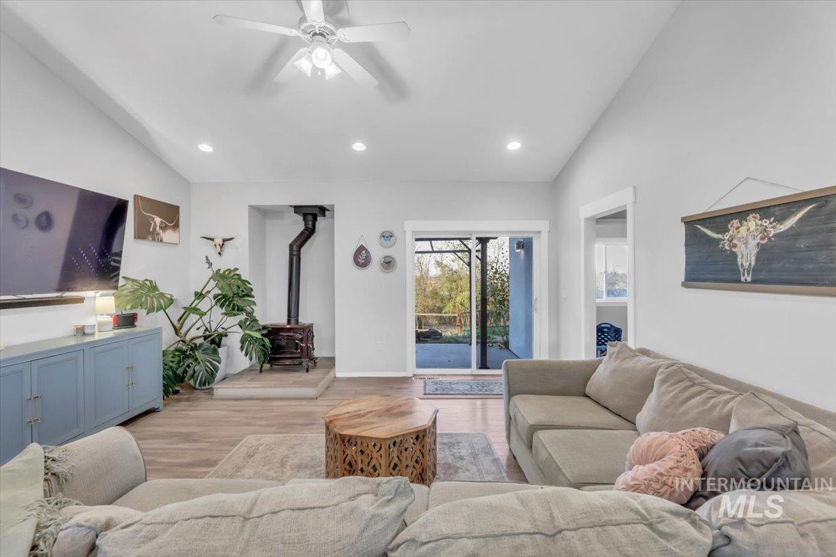 Living area featuring vaulted ceiling, a wood stove, wood finished floors, recessed lighting, and ceiling fan