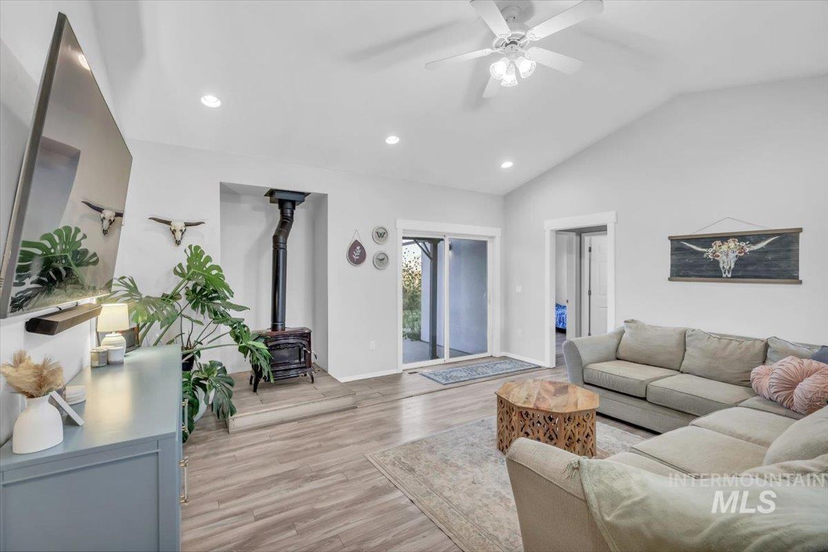 Living area with a wood stove, light wood-type flooring, recessed lighting, ceiling fan, and vaulted ceiling