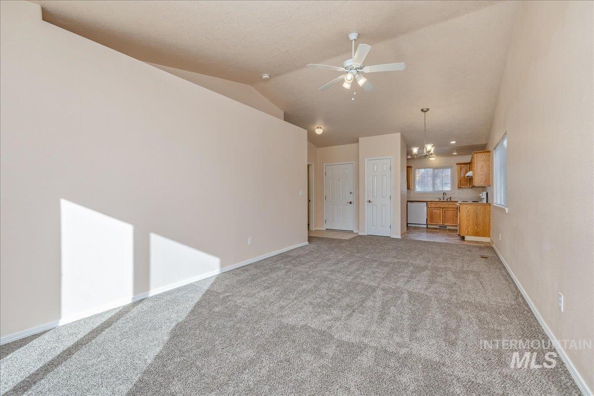 Unfurnished living room with light colored carpet, lofted ceiling, a ceiling fan, and a chandelier