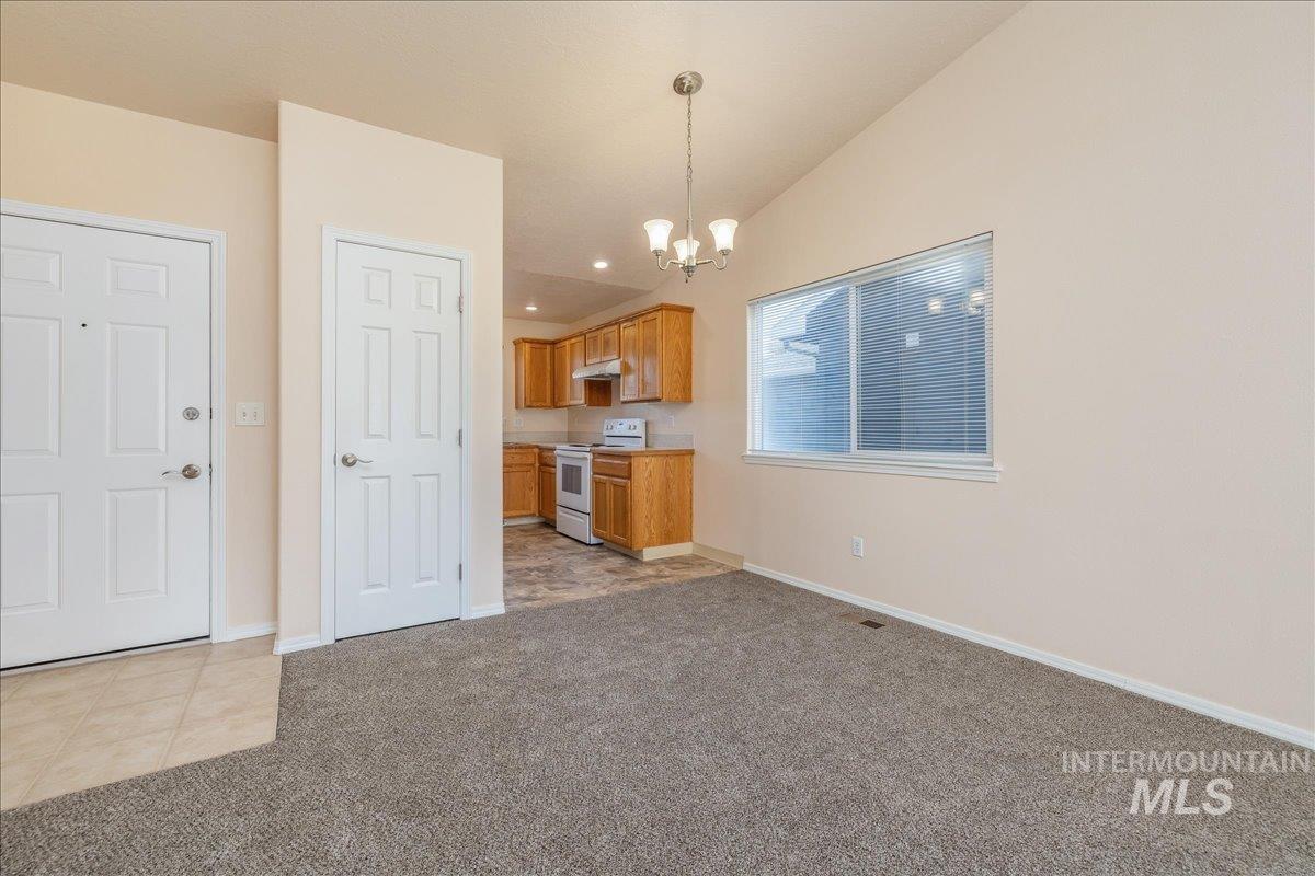 Kitchen with white electric range oven, light carpet, vaulted ceiling, pendant lighting, and brown cabinets