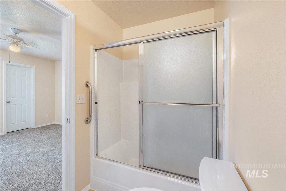 Full bath featuring carpet floors, bath / shower combo with glass door, a textured ceiling, and ceiling fan