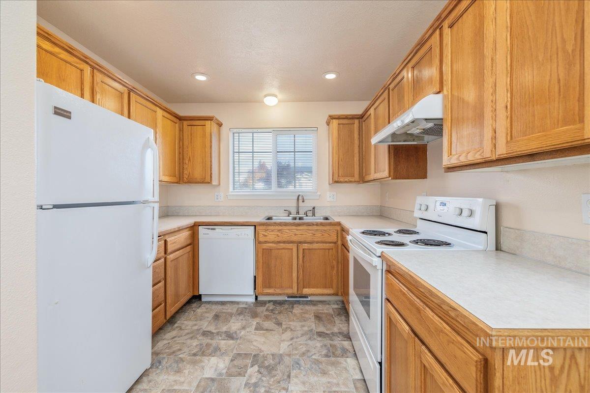 Kitchen featuring white appliances, light countertops, under cabinet range hood, stone finish flooring, and brown cabinetry