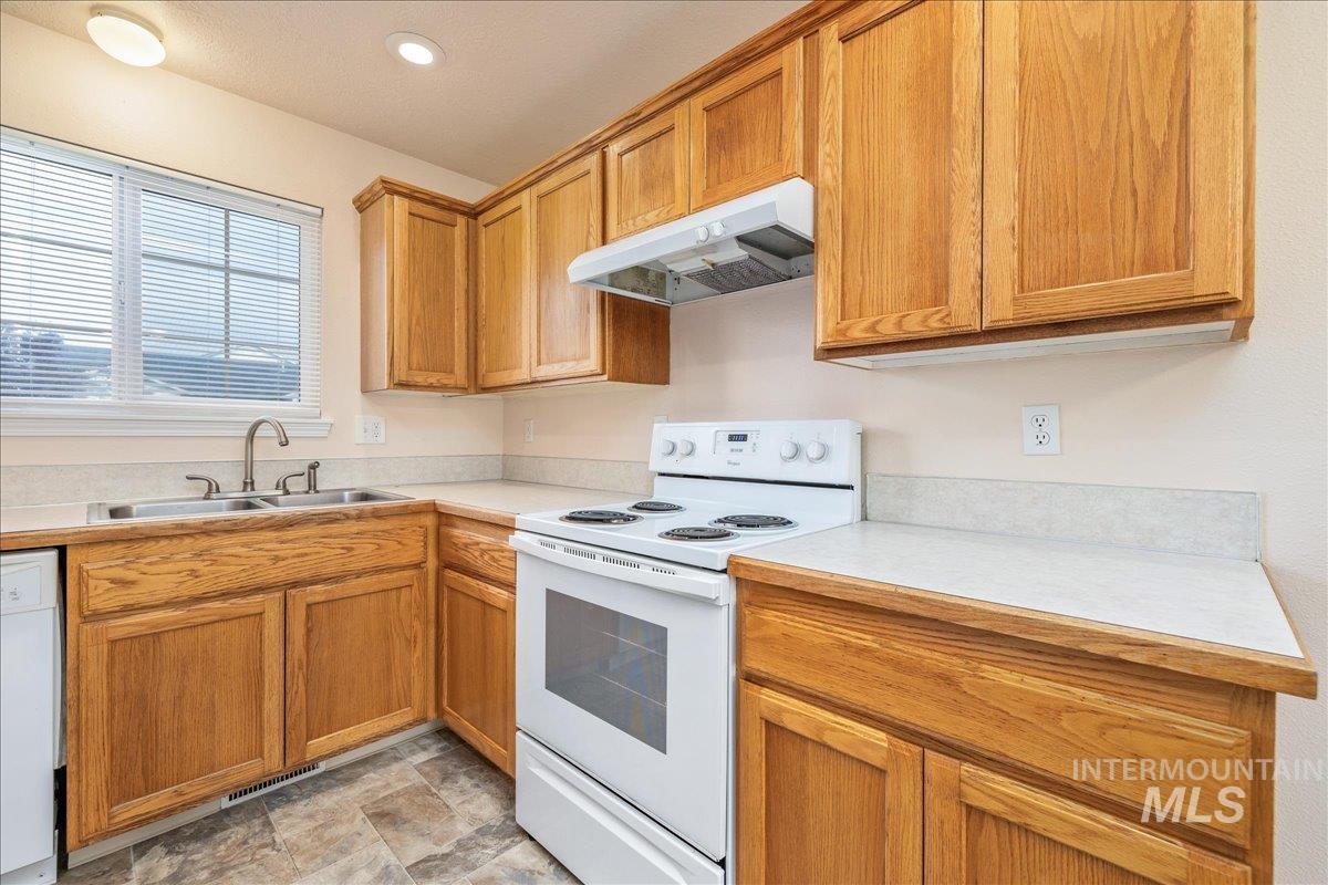 Kitchen with white appliances, light countertops, under cabinet range hood, brown cabinetry, and stone finish floors