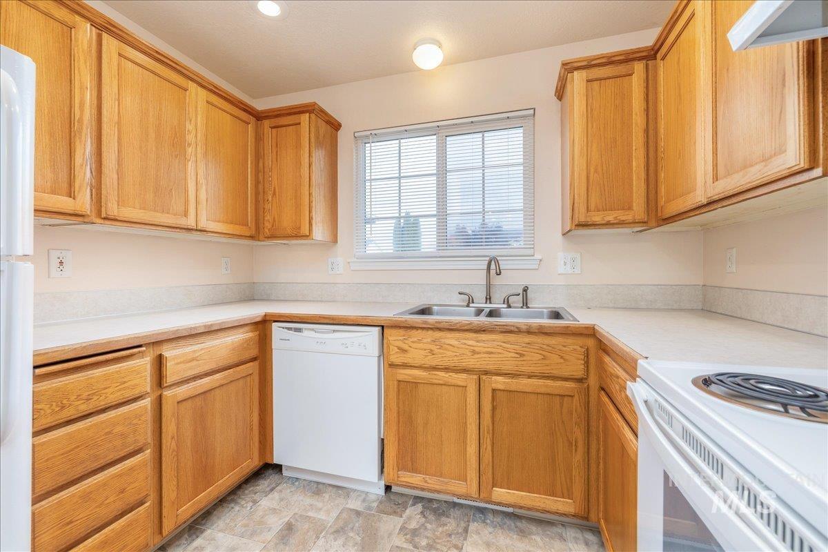 Kitchen with light countertops, white appliances, range hood, and stone finish flooring