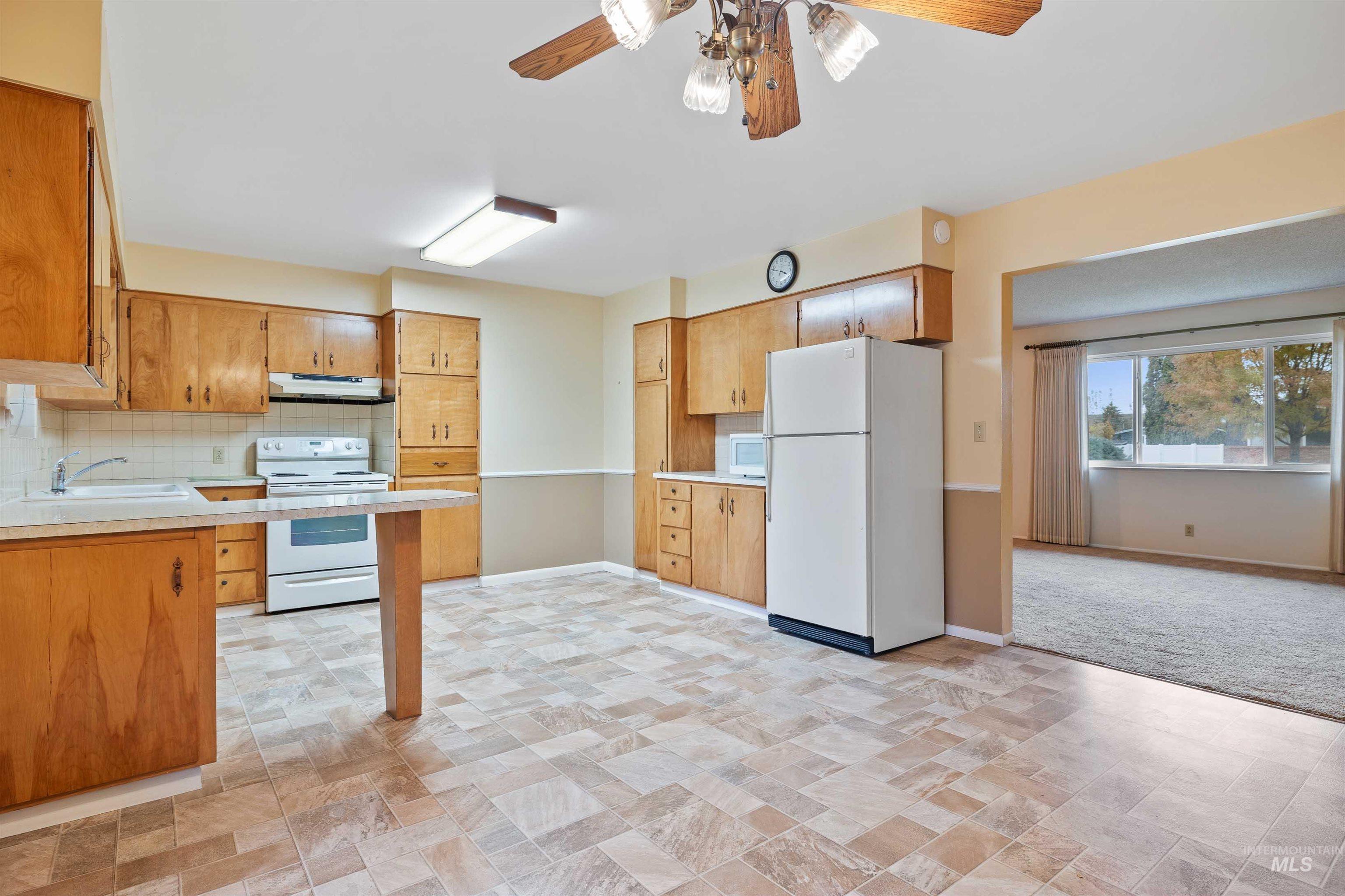 Kitchen with tasteful backsplash, white appliances, light countertops, ceiling fan, and brown cabinetry