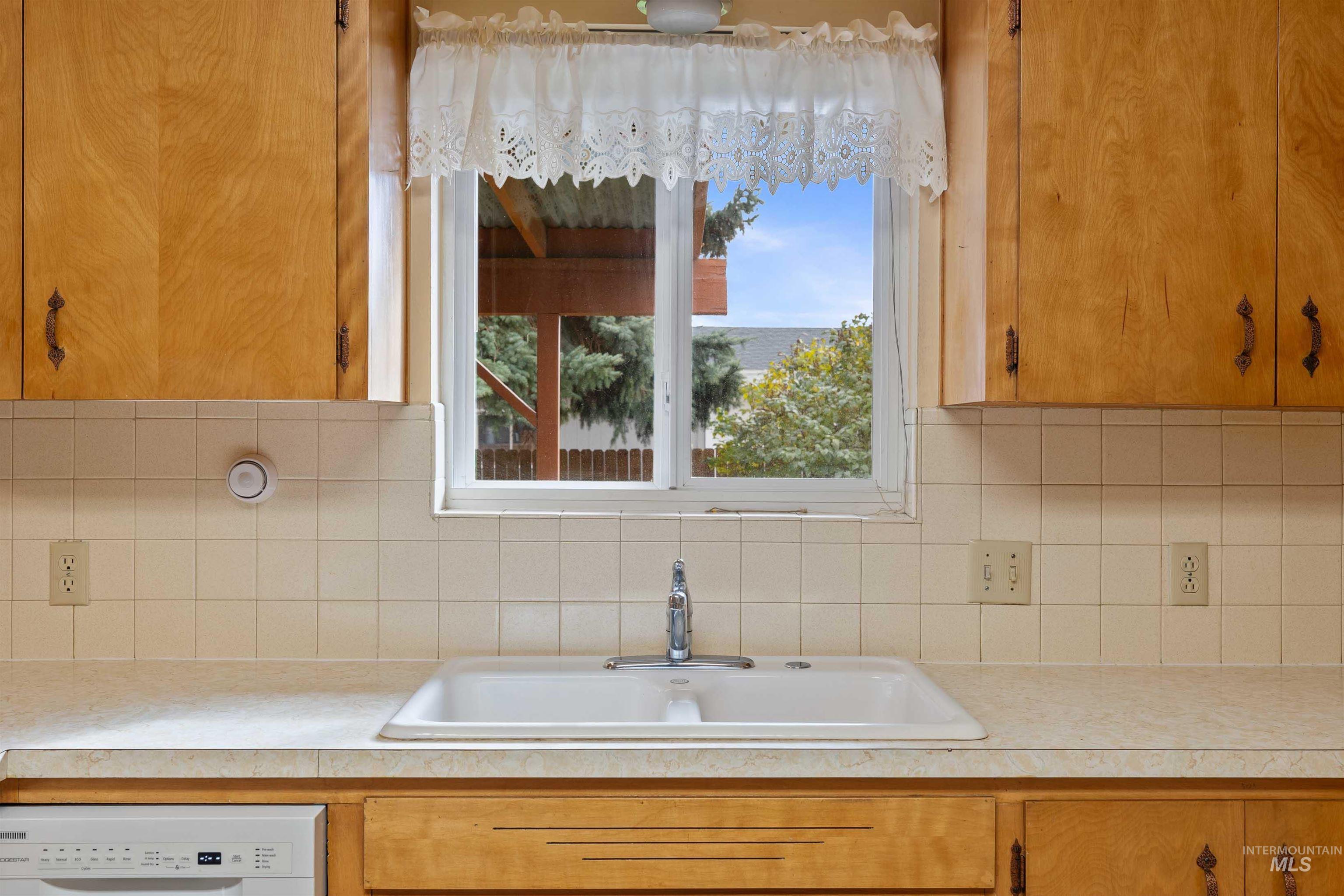 Kitchen featuring light countertops, tasteful backsplash, white dishwasher, and brown cabinets