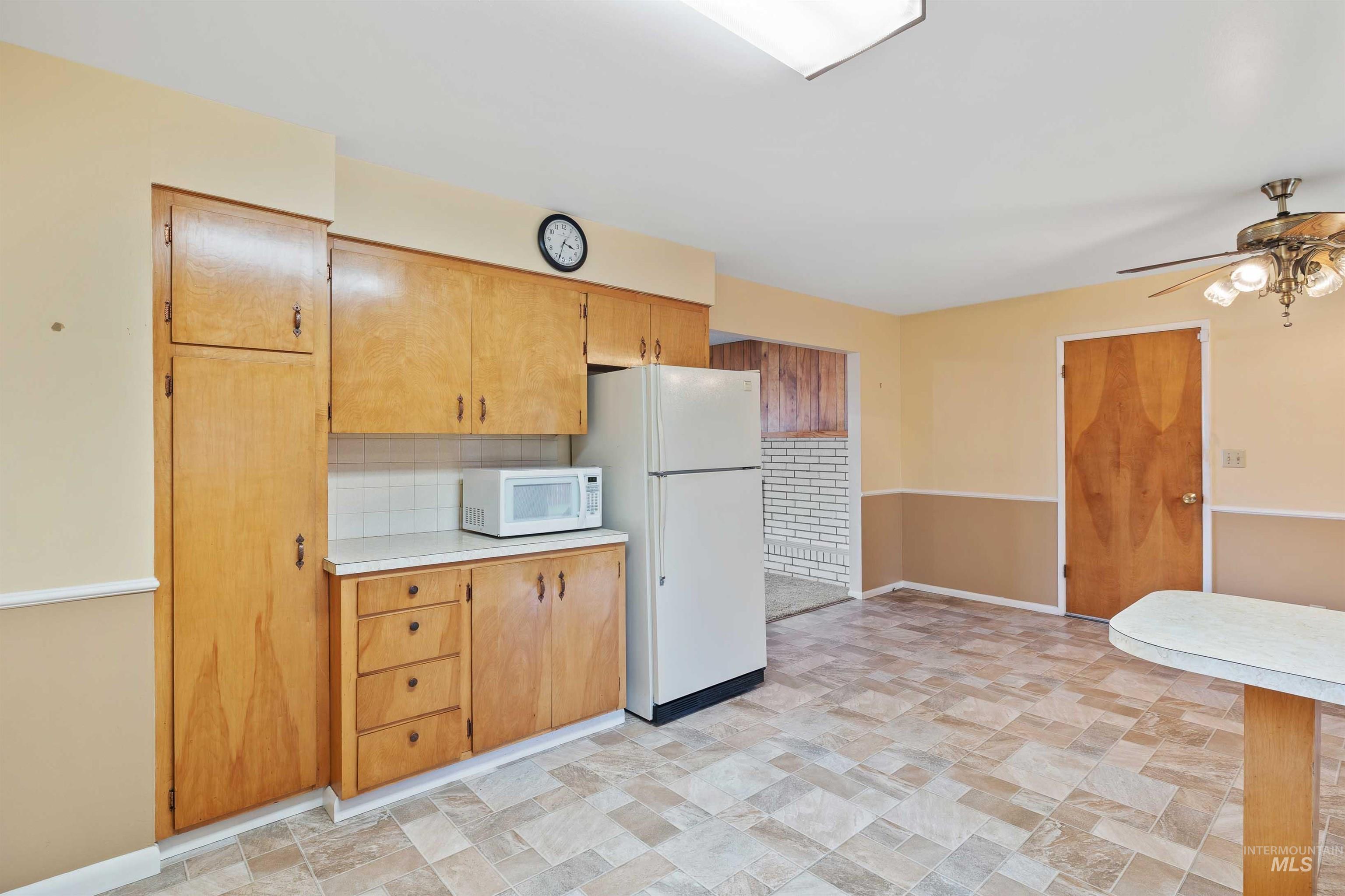 Kitchen featuring light countertops, backsplash, white appliances, ceiling fan, and stone finish floors