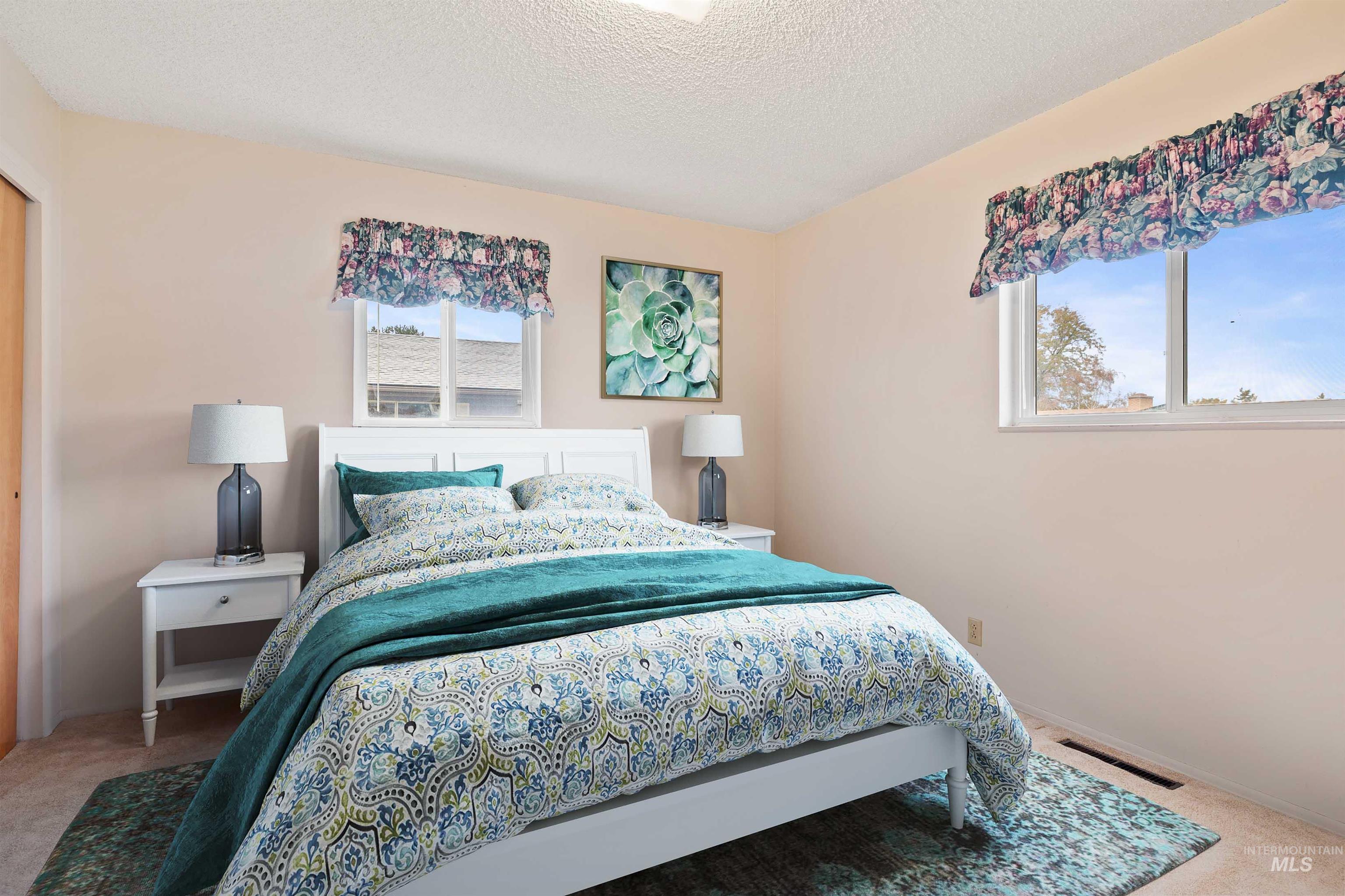 Bedroom featuring light colored carpet, a textured ceiling, multiple windows, and a closet