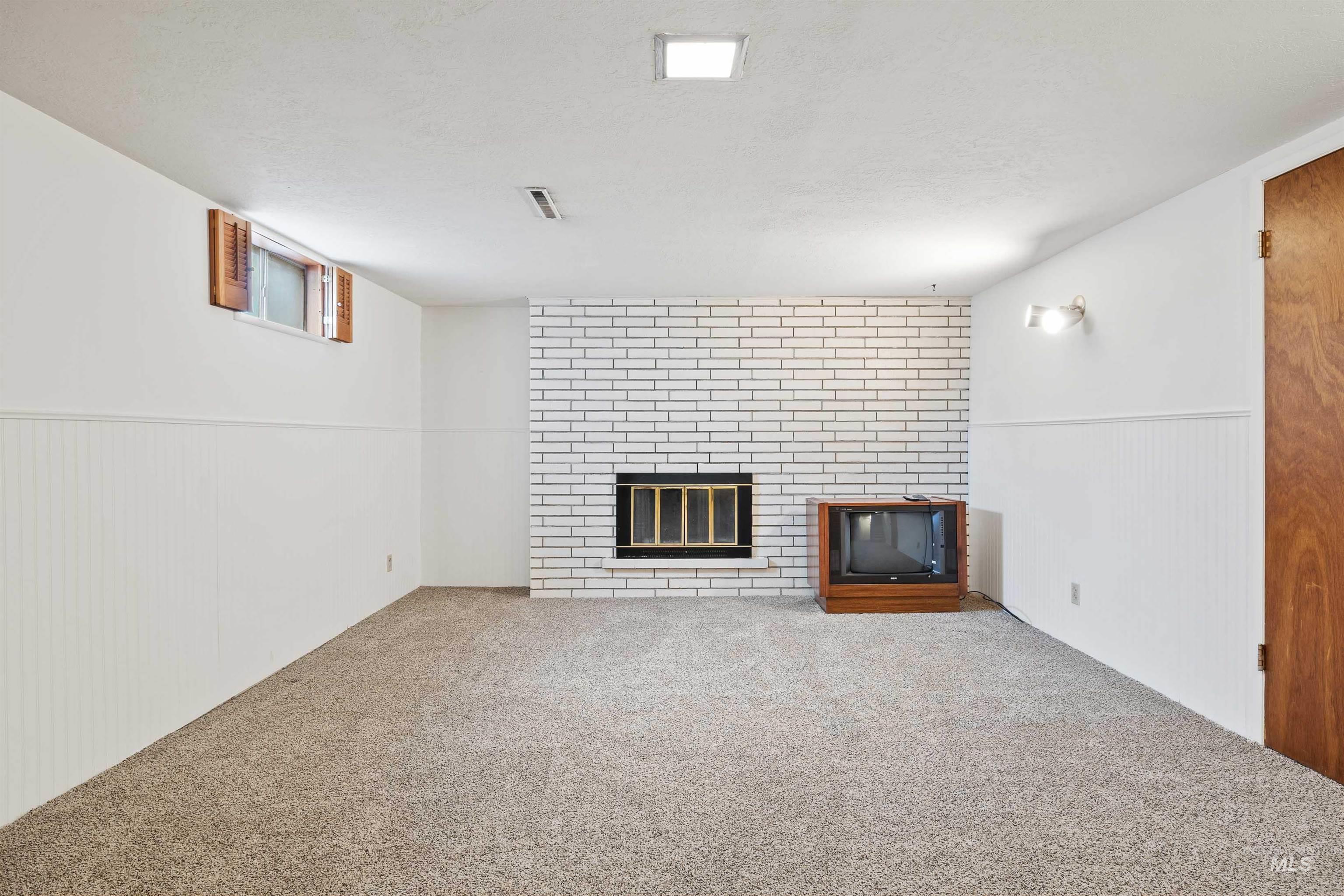 Unfurnished living room featuring a wainscoted wall, carpet flooring, a brick fireplace, a textured ceiling, and wooden walls
