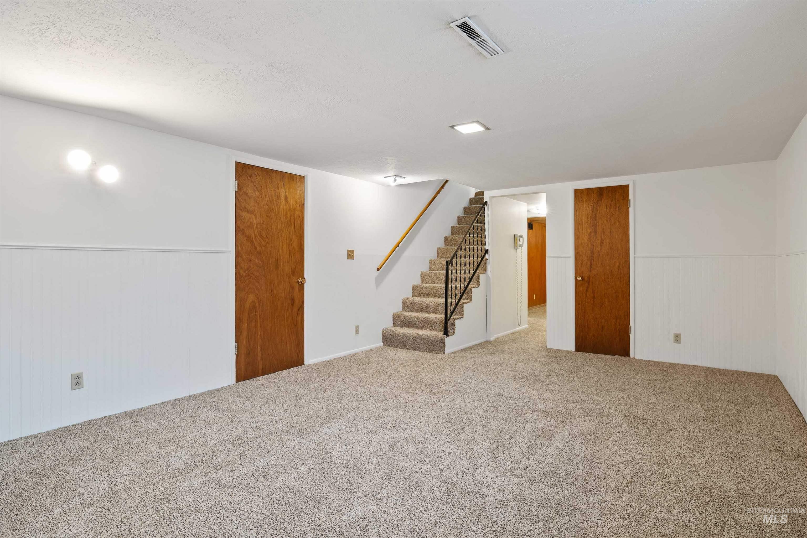 Finished basement featuring stairs, carpet flooring, a textured ceiling, wainscoting, and wood walls
