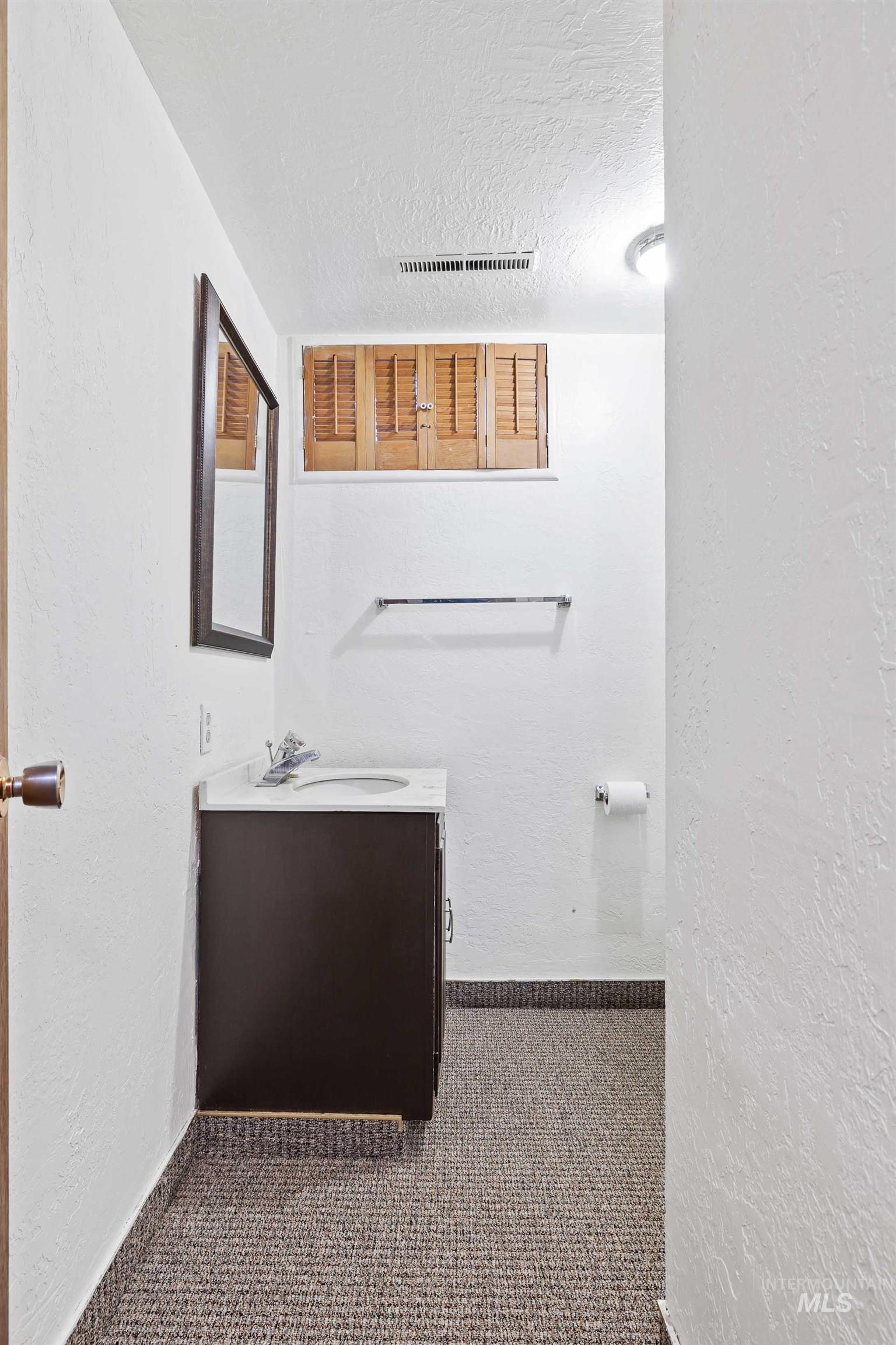 Half bath with a textured wall, vanity, and a textured ceiling