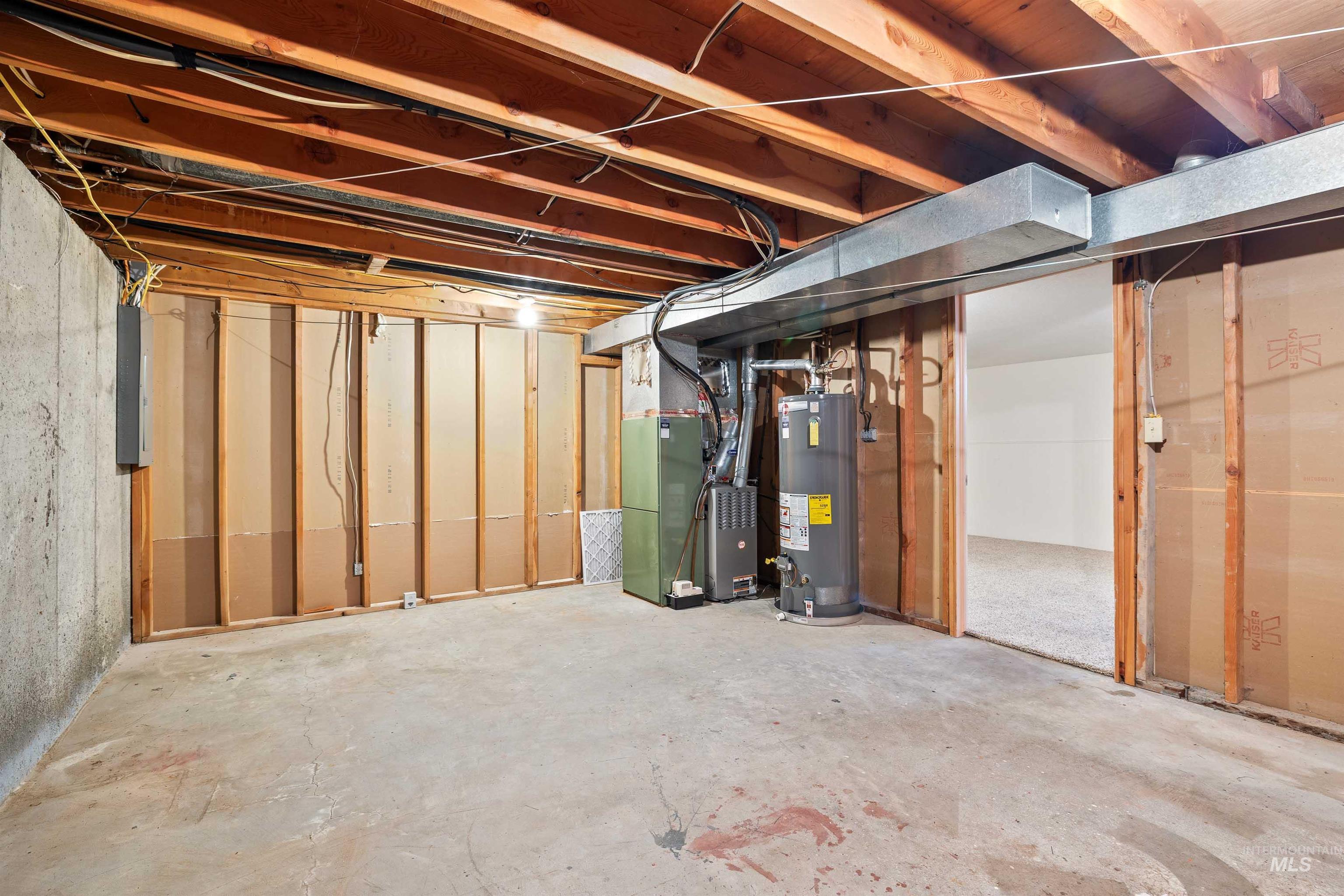 Unfinished below grade area featuring heating unit, water heater, and electric panel