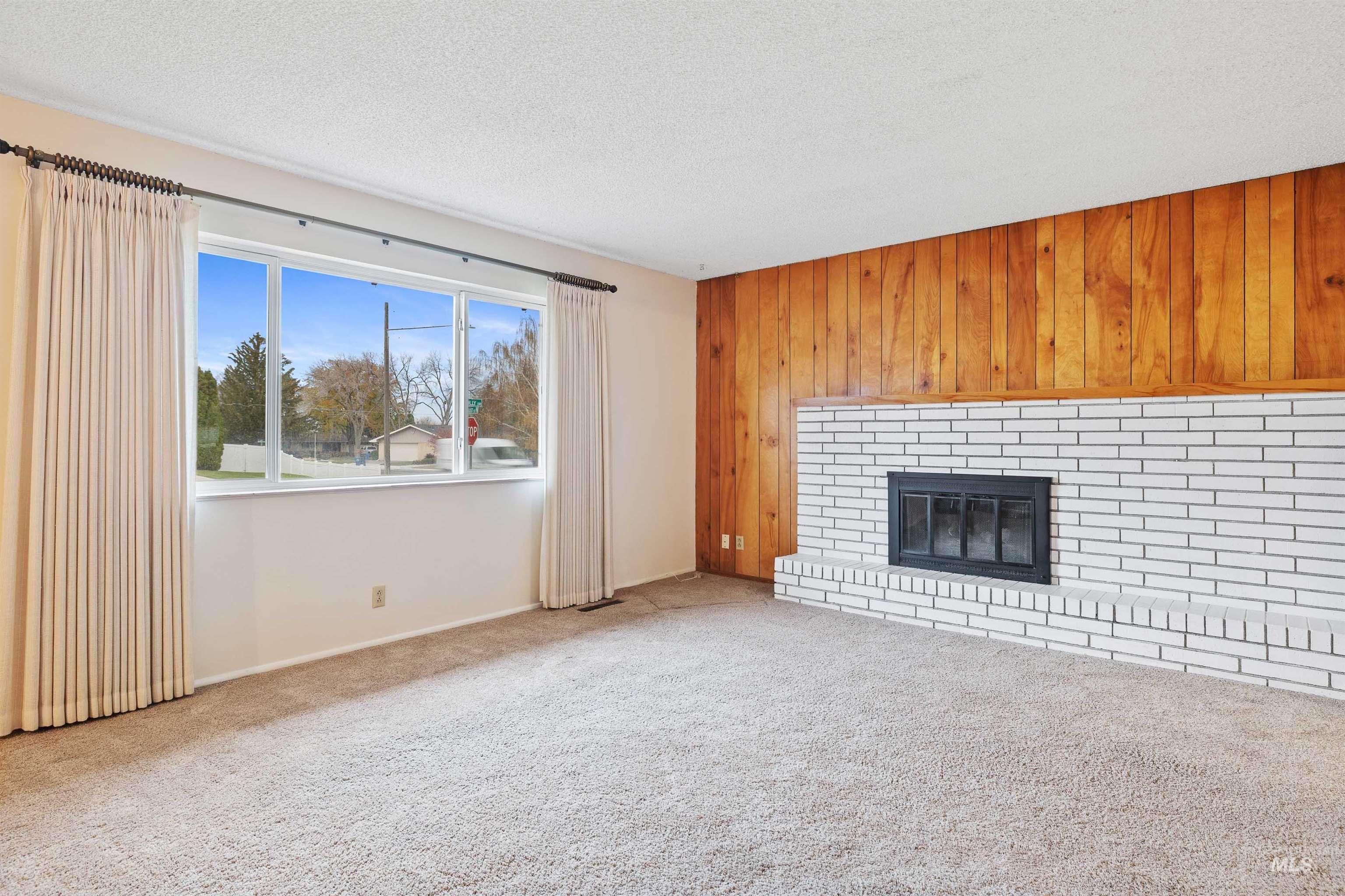 Unfurnished living room with wooden walls, a brick fireplace, carpet, and a textured ceiling
