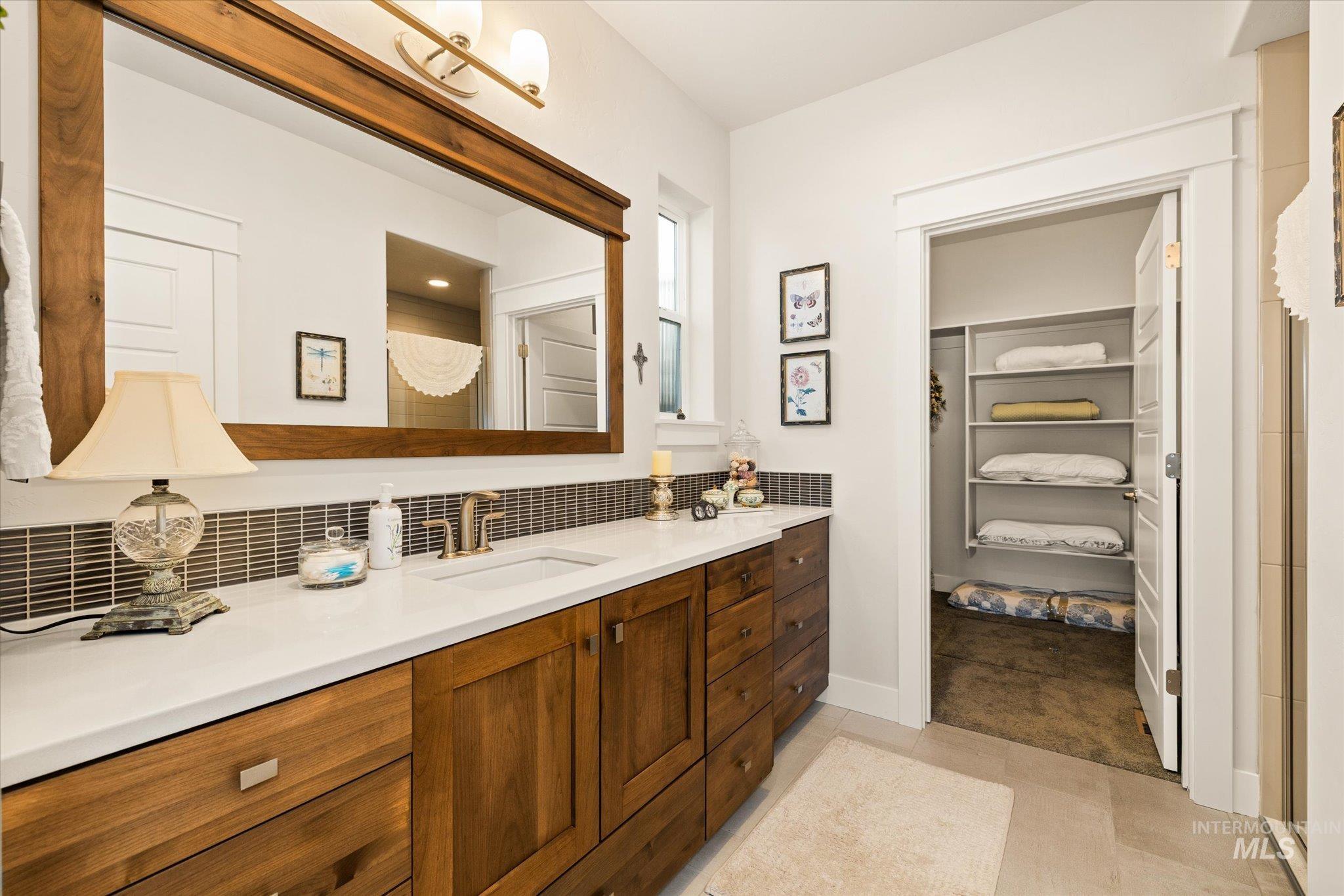 Full bath featuring a shower stall, a walk in closet, vanity, light tile patterned floors, and decorative backsplash