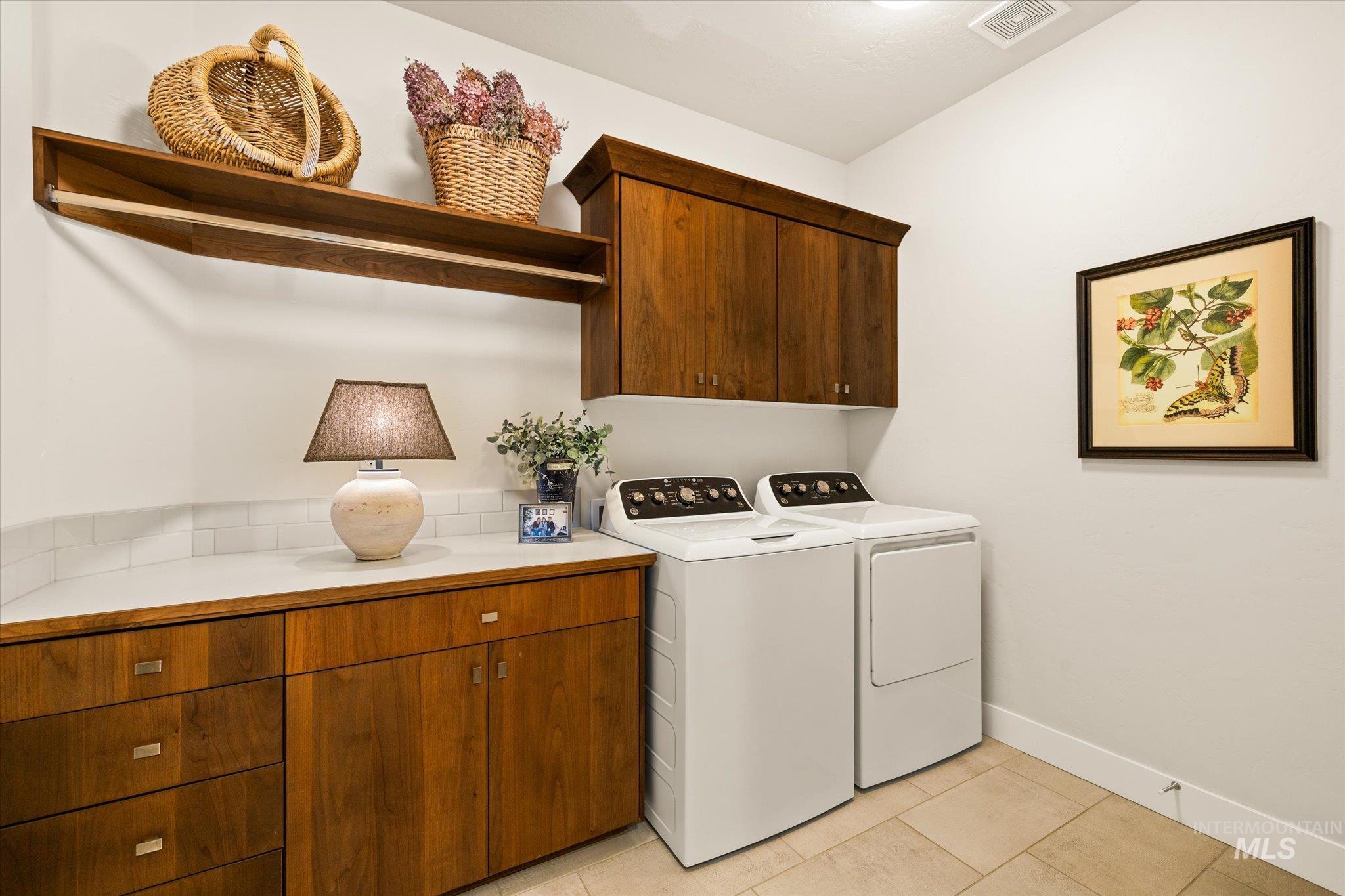 Washroom featuring light tile patterned floors, washing machine and clothes dryer, and cabinet space