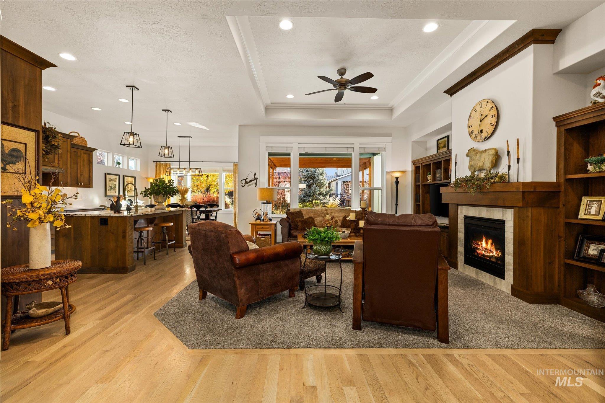 Living area featuring a tray ceiling, a tile fireplace, light wood-style floors, recessed lighting, and a ceiling fan