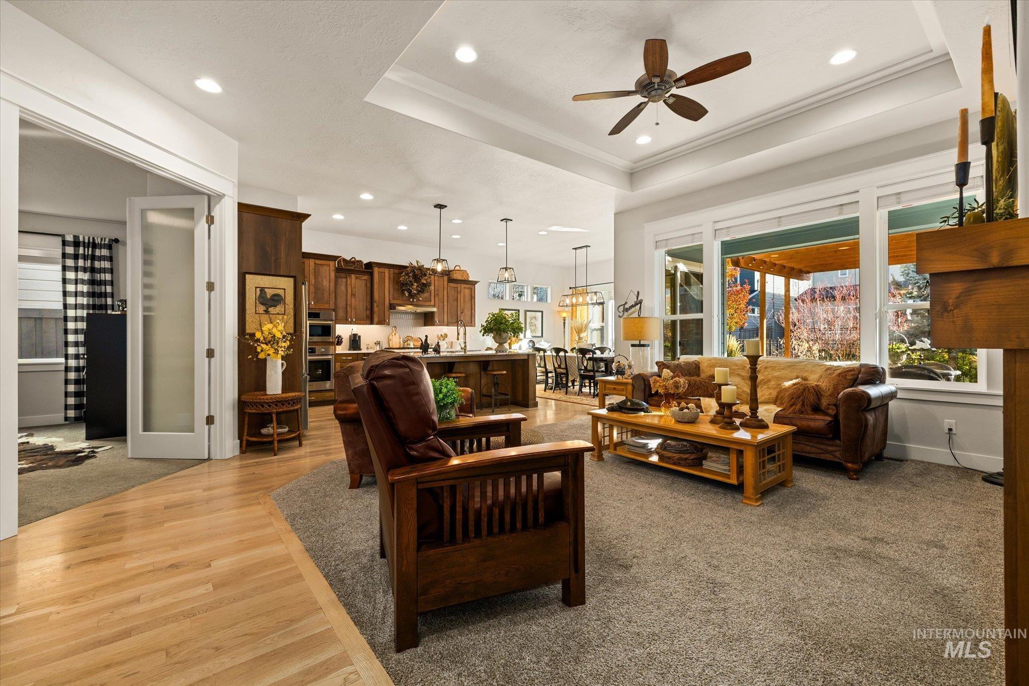 Living area featuring a raised ceiling, recessed lighting, a ceiling fan, light carpet, and light wood-style floors