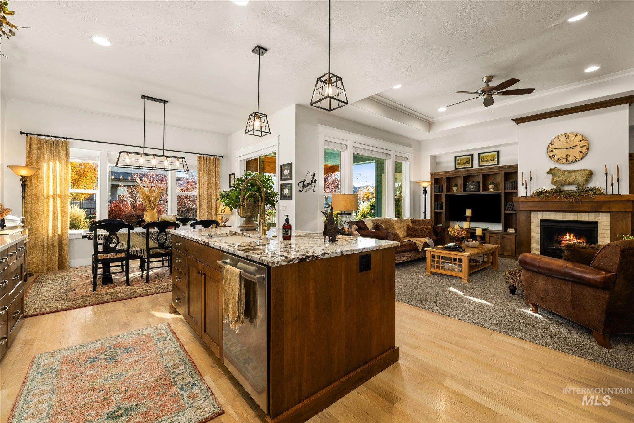 Kitchen featuring decorative light fixtures, a tray ceiling, a fireplace, recessed lighting, and light stone countertops