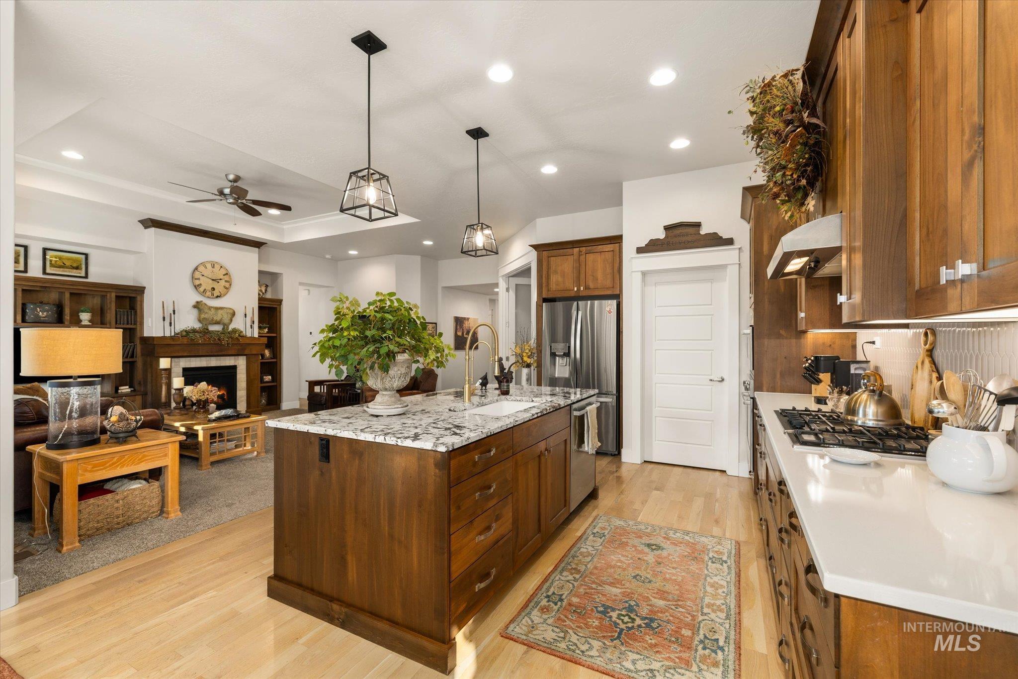 Kitchen featuring decorative light fixtures, a tile fireplace, a ceiling fan, light wood-style floors, and light stone counters