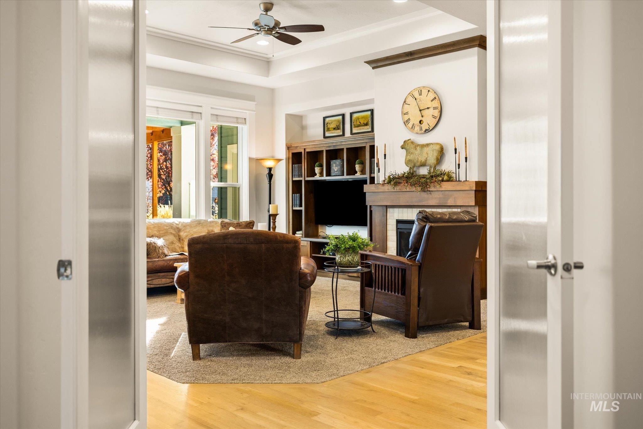 Living area featuring wood finished floors, a fireplace, a ceiling fan, ornamental molding, and a raised ceiling