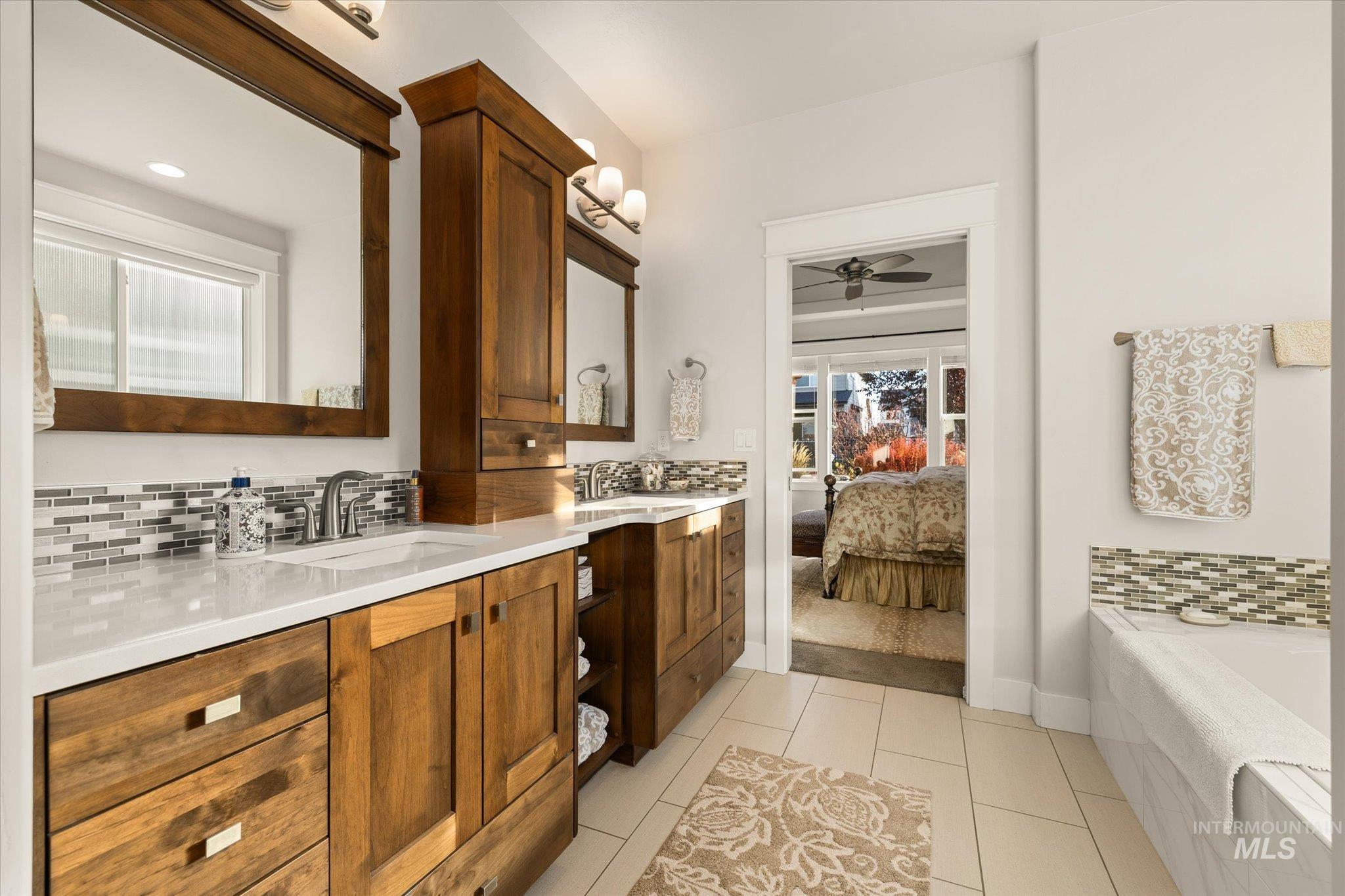Ensuite bathroom with backsplash, double vanity, light tile patterned flooring, and ceiling fan