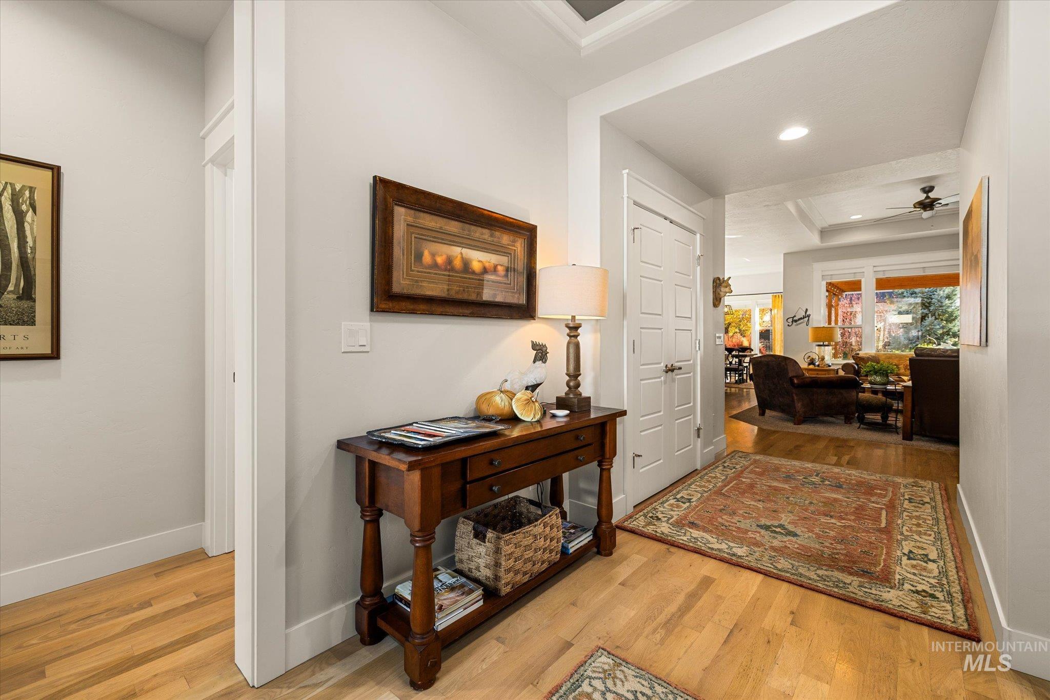Corridor with light wood finished floors, a tray ceiling, and recessed lighting