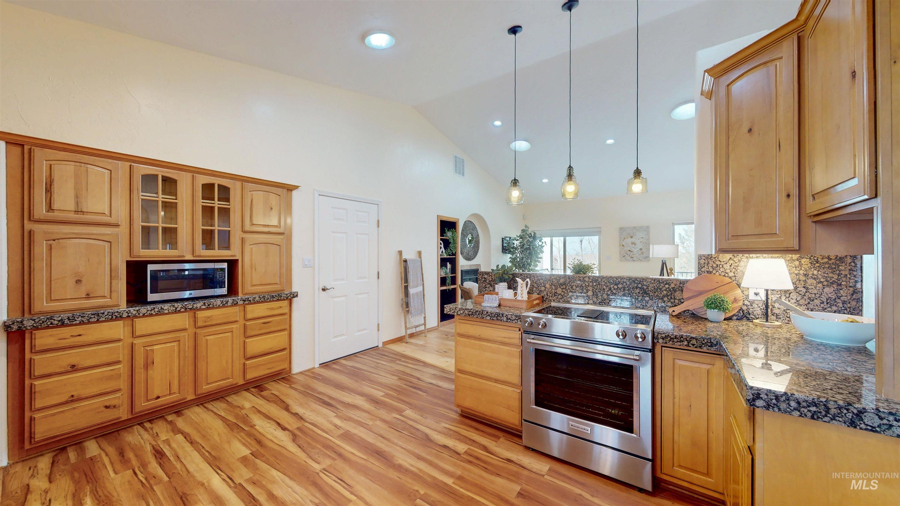 Kitchen with stainless steel appliances, a peninsula, pendant lighting, backsplash, and light wood finished floors