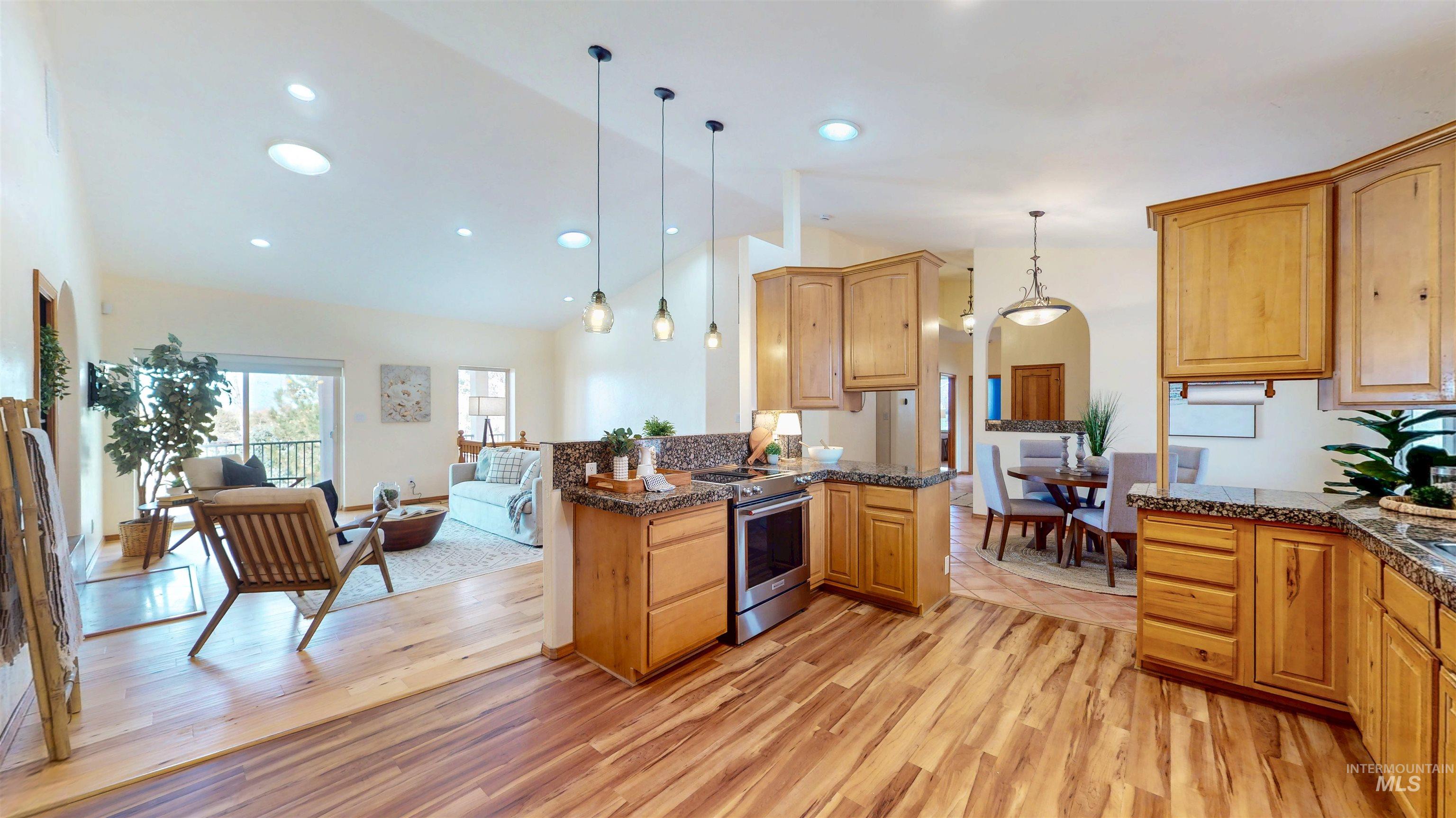 Kitchen with open floor plan, hanging light fixtures, electric range, light wood-style floors, and recessed lighting