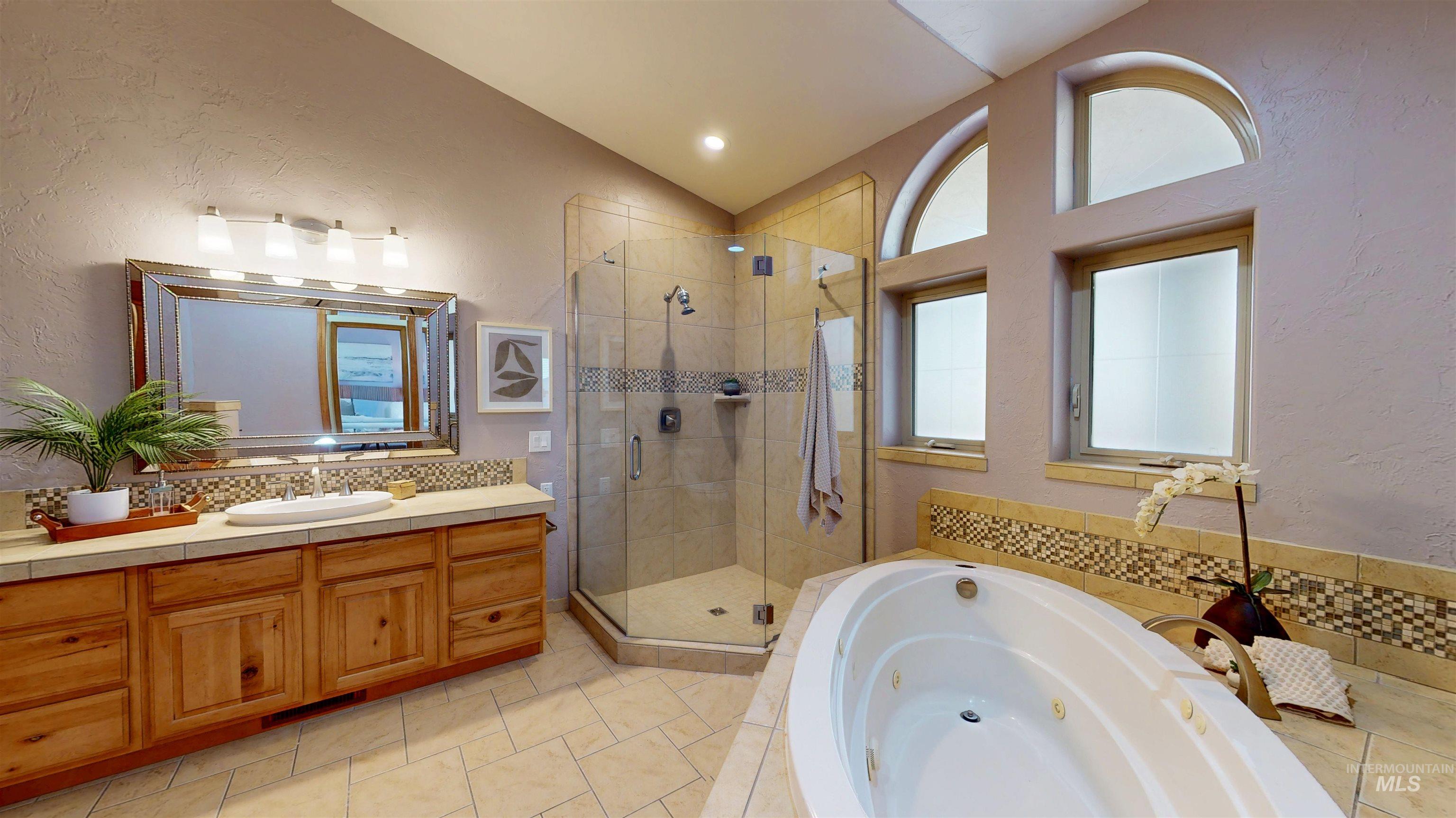 Full bath with a textured wall, a tub with jets, vanity, a shower stall, and lofted ceiling