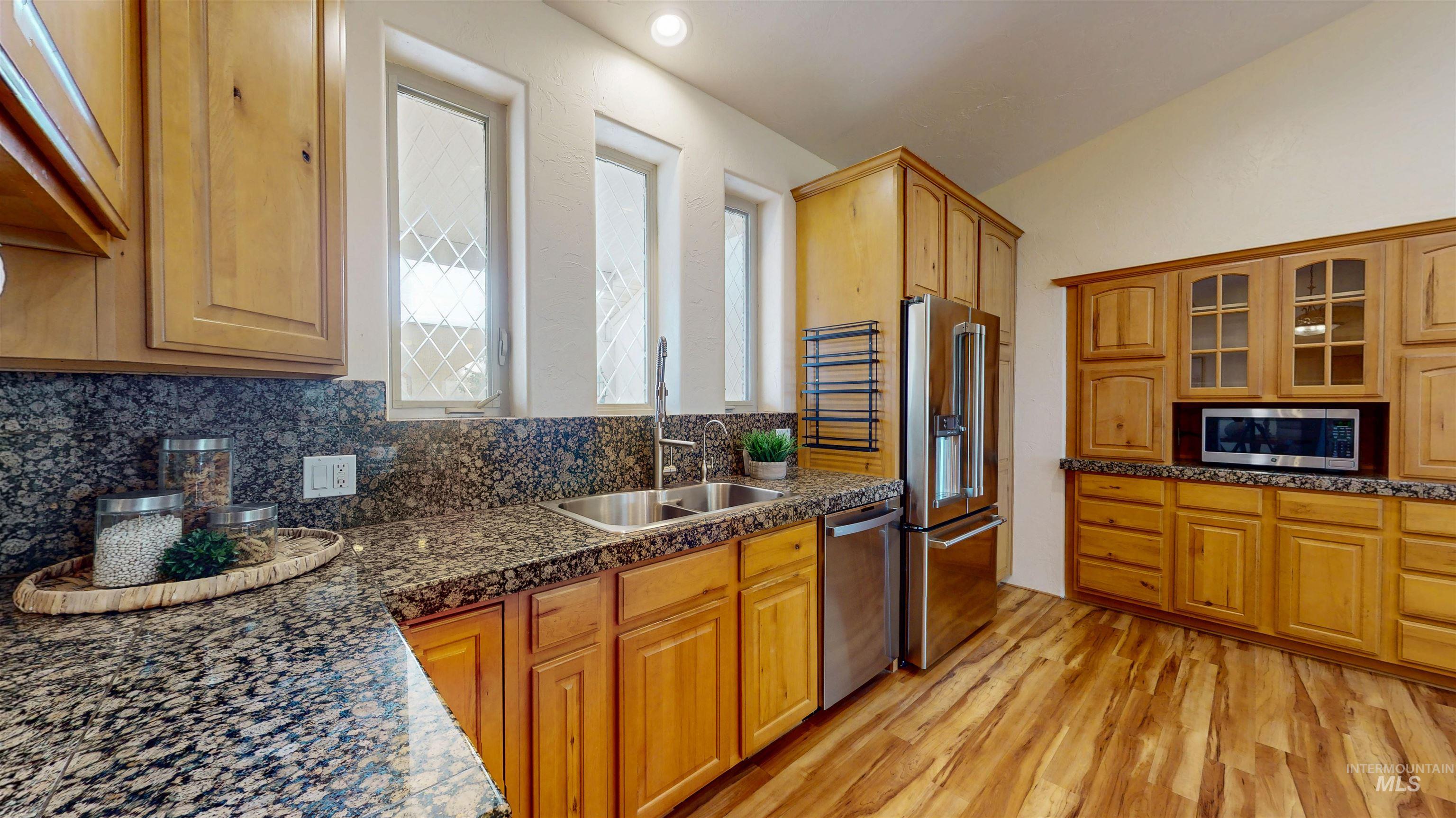 Kitchen featuring backsplash, stainless steel appliances, light wood finished floors, and glass insert cabinets