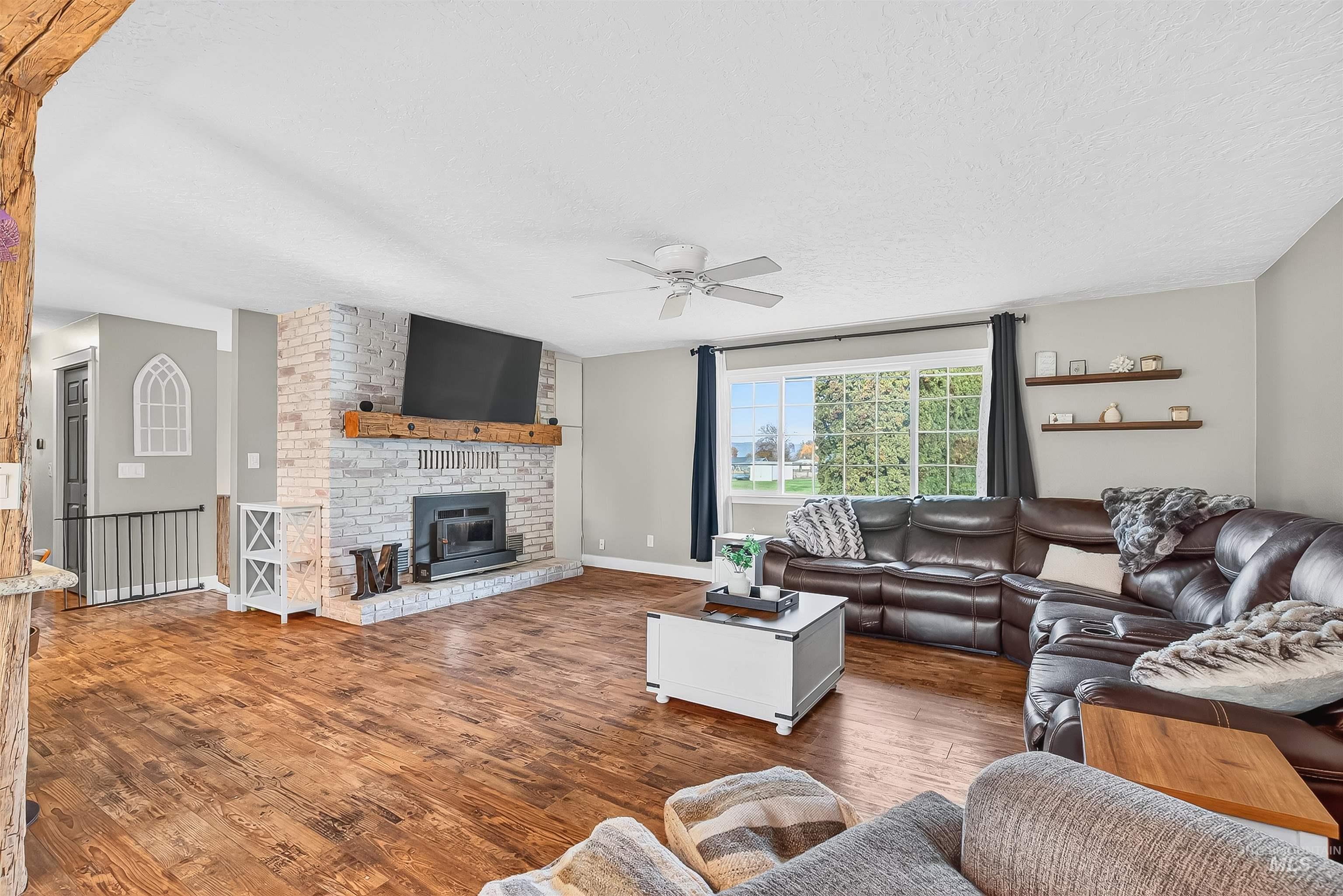 Living room with wood finished floors, a brick fireplace, a textured ceiling, and a ceiling fan
