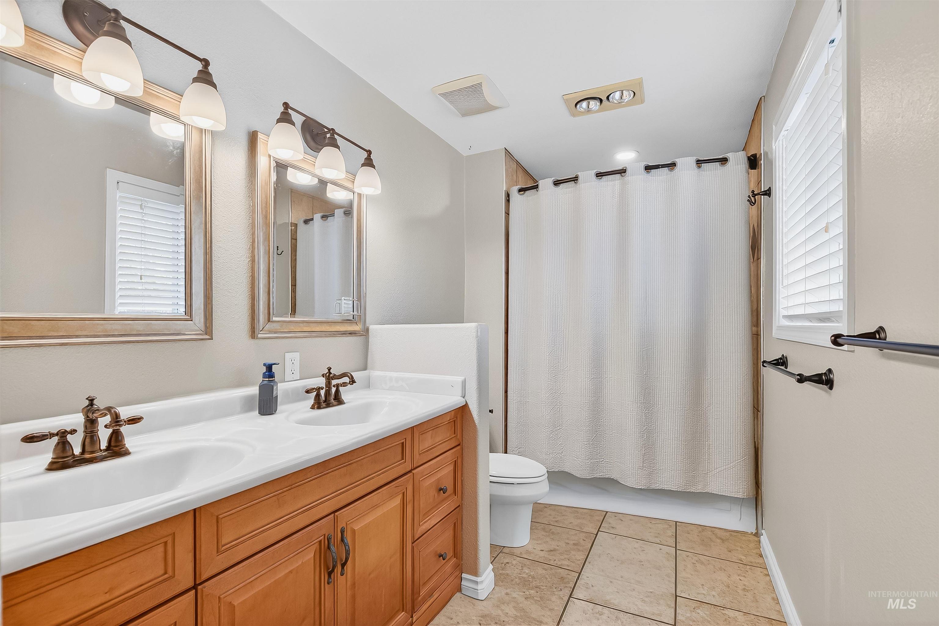 Full bathroom featuring double vanity, light tile patterned floors, and shower / bath combination with curtain
