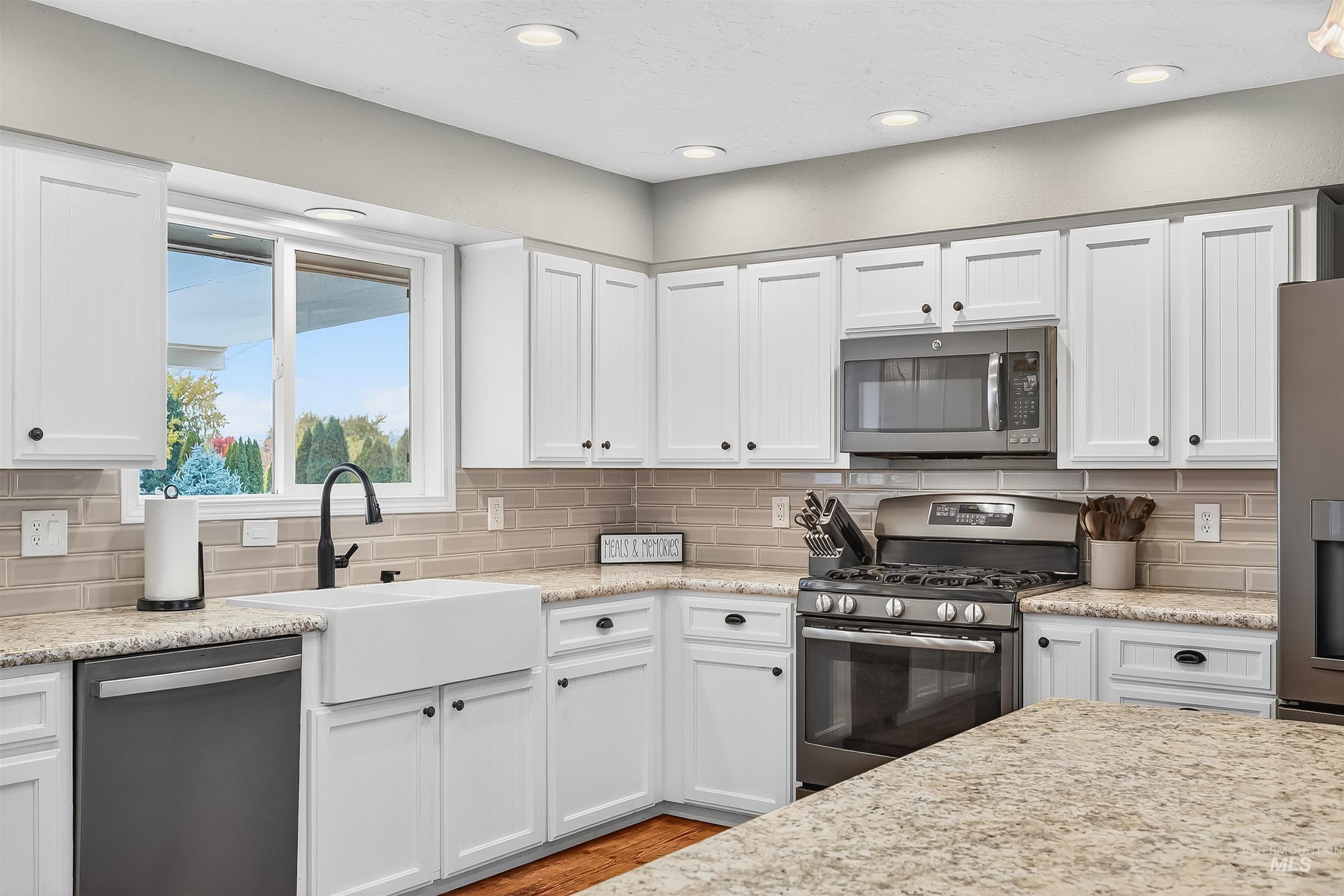 Kitchen featuring white cabinetry, stainless steel appliances, decorative backsplash, light stone countertops, and recessed lighting