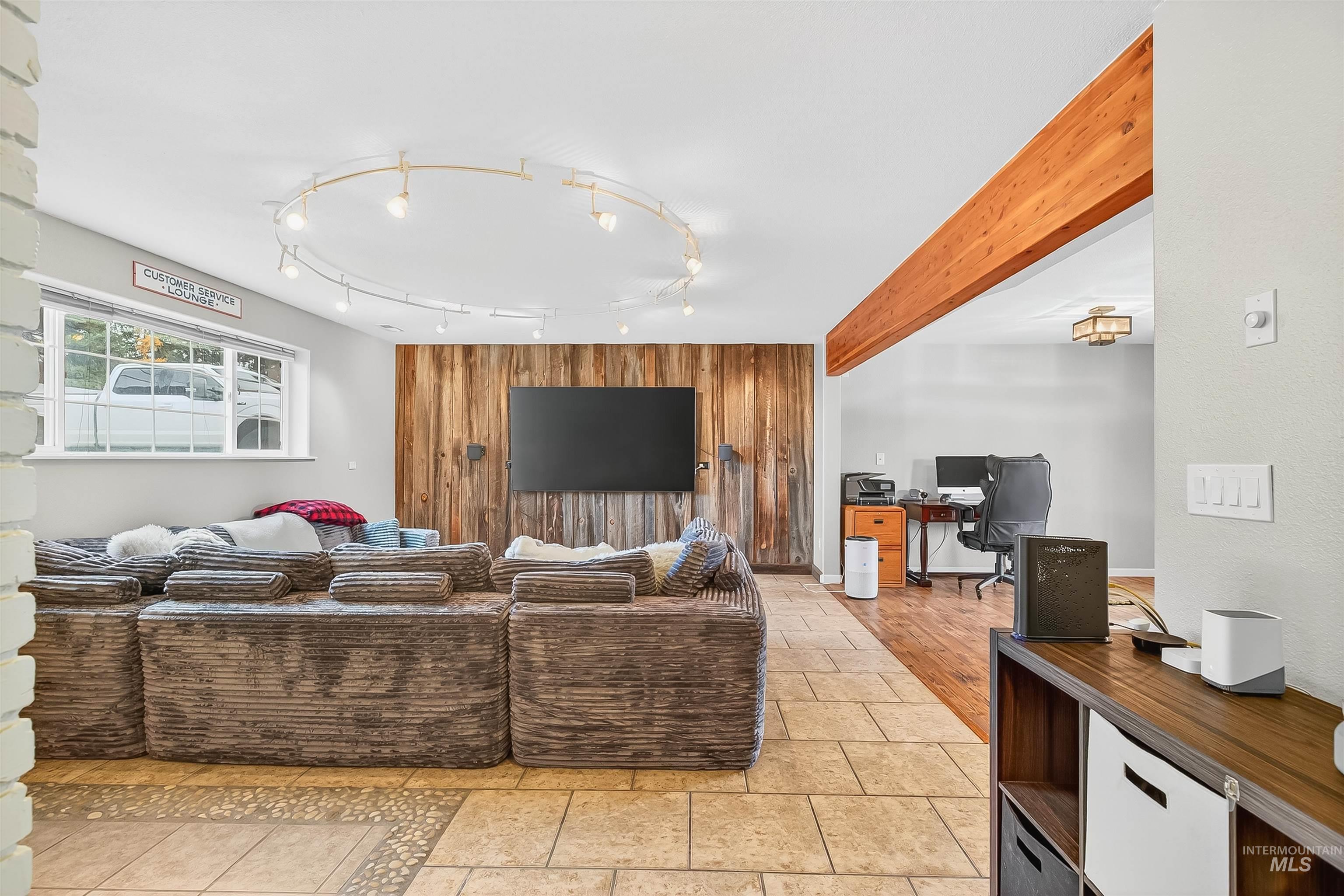 Living area featuring a desk, wood walls, light tile patterned floors, and beam ceiling