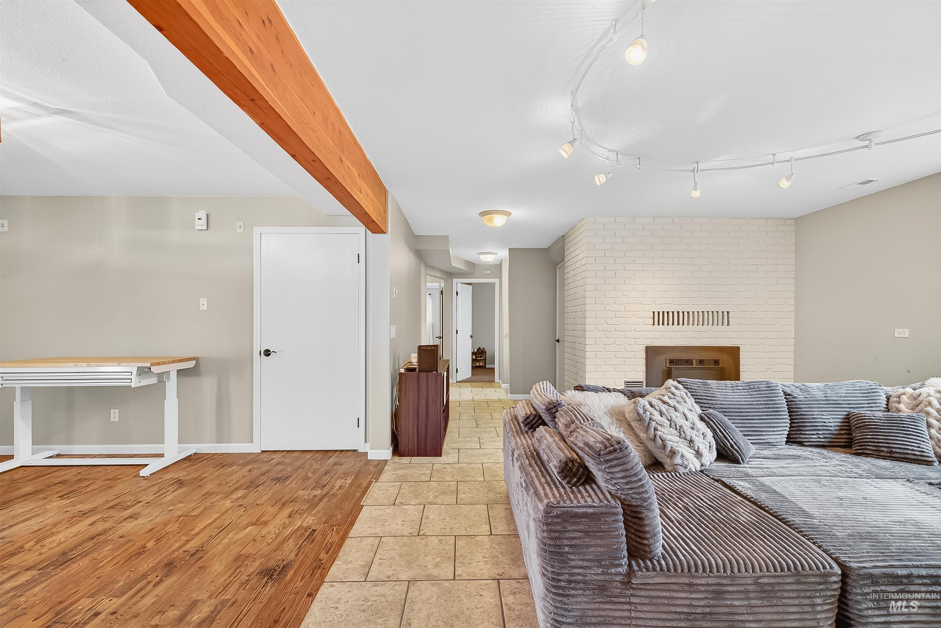 Living area with light wood-type flooring, a brick fireplace, and beam ceiling