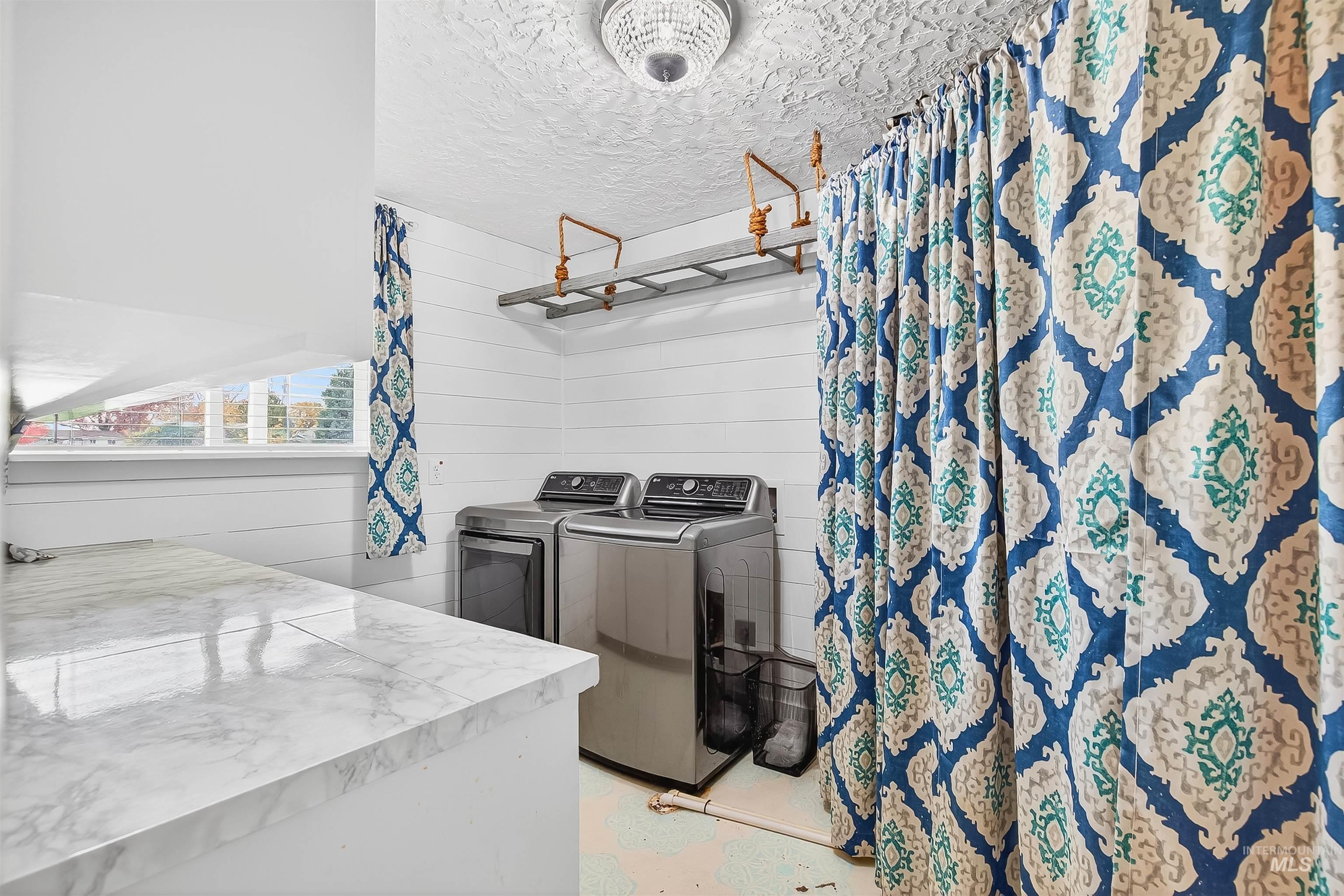 Laundry area featuring a textured ceiling, independent washer and dryer, and wooden walls