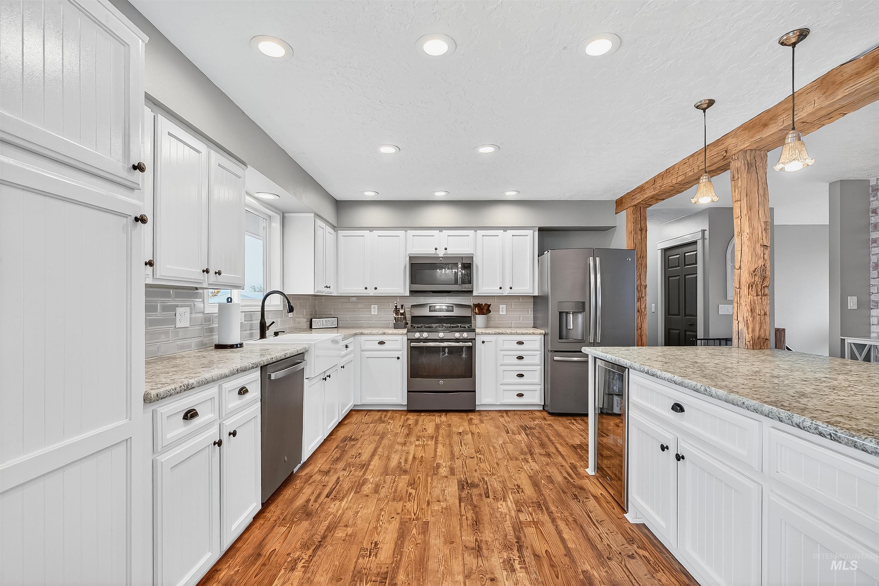 Kitchen featuring white cabinets, stainless steel appliances, light wood-style floors, decorative light fixtures, and tasteful backsplash