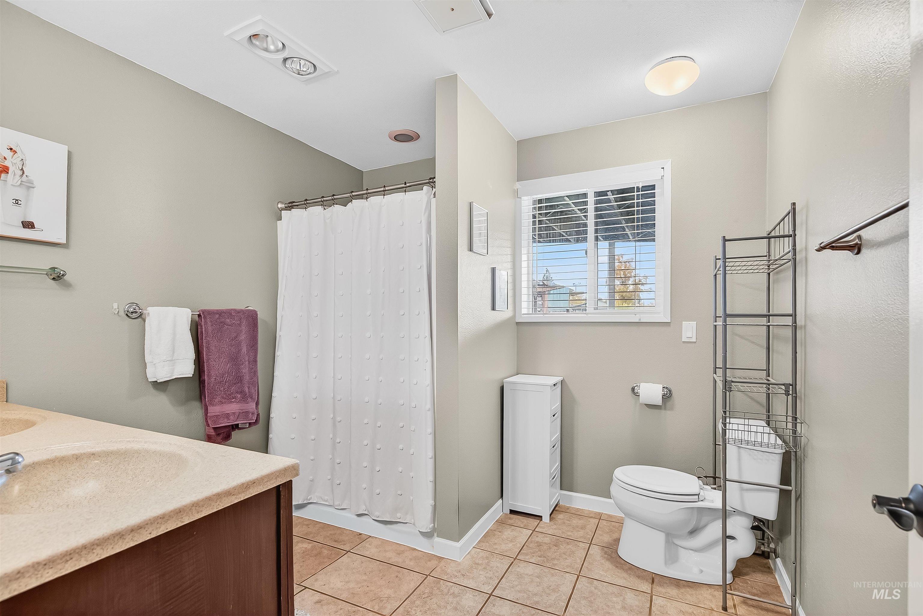 Bathroom with curtained shower, light tile patterned floors, and double vanity
