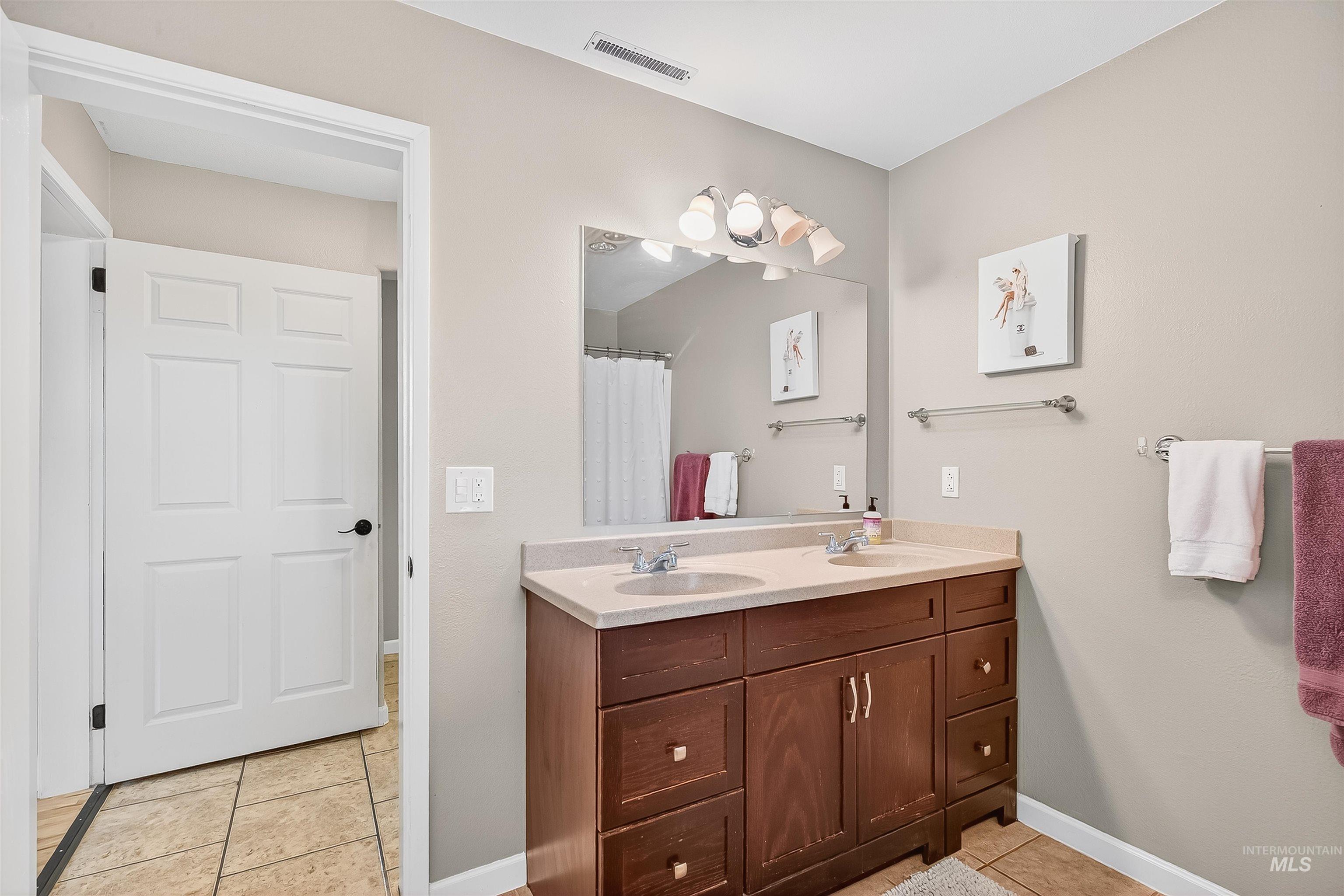 Bathroom with light tile patterned floors, double vanity, and a shower with curtain