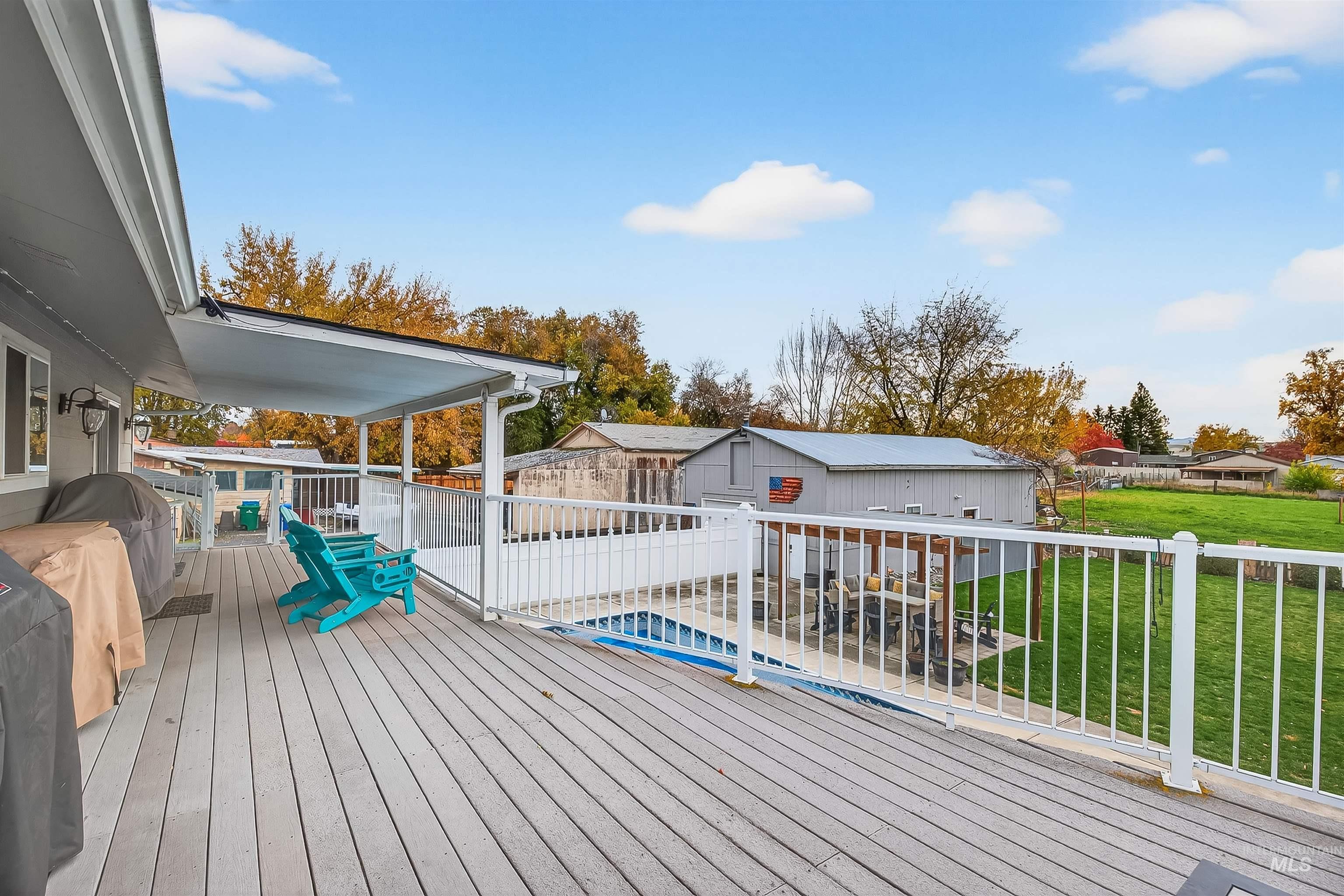 Wooden terrace with a lawn, a grill, an outbuilding, and a residential view