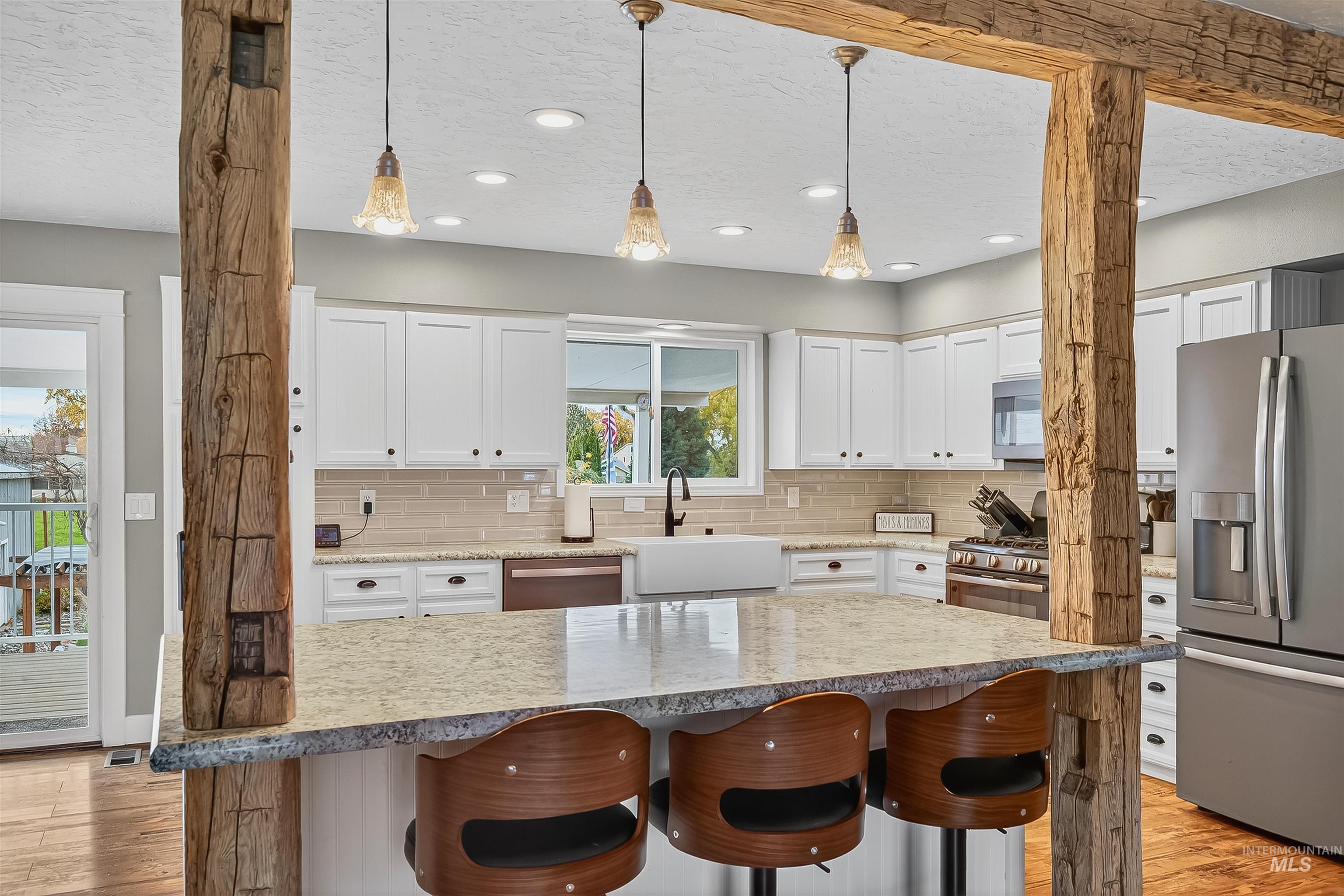 Kitchen featuring white cabinets, appliances with stainless steel finishes, light wood-type flooring, hanging light fixtures, and a textured ceiling