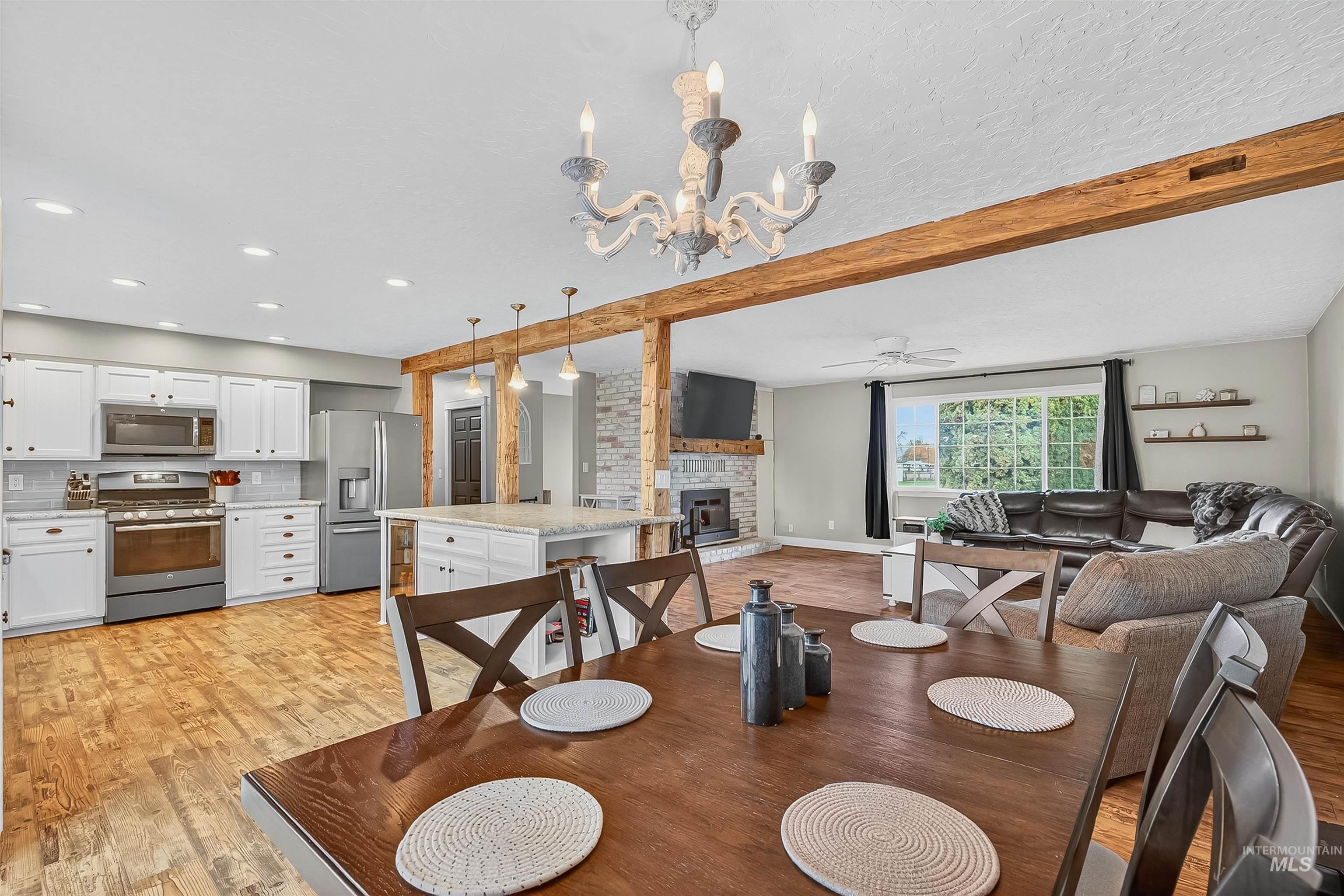 Dining space featuring beamed ceiling, light wood finished floors, a stone fireplace, a chandelier, and a ceiling fan