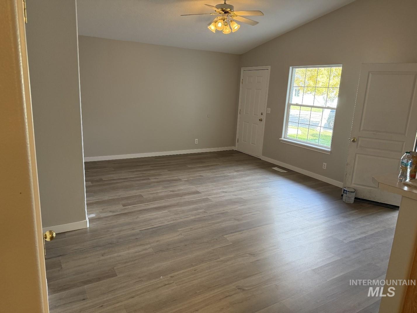 Empty room with vaulted ceiling, light wood-type flooring, and a ceiling fan