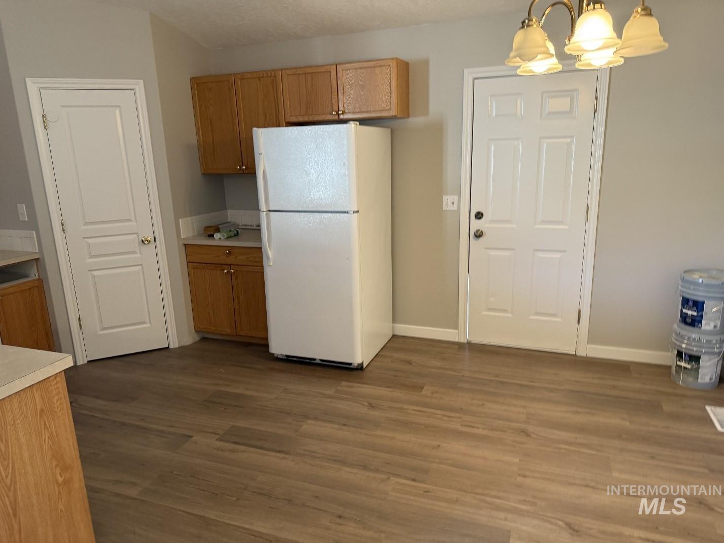 Kitchen with freestanding refrigerator, light countertops, a chandelier, dark wood finished floors, and brown cabinetry