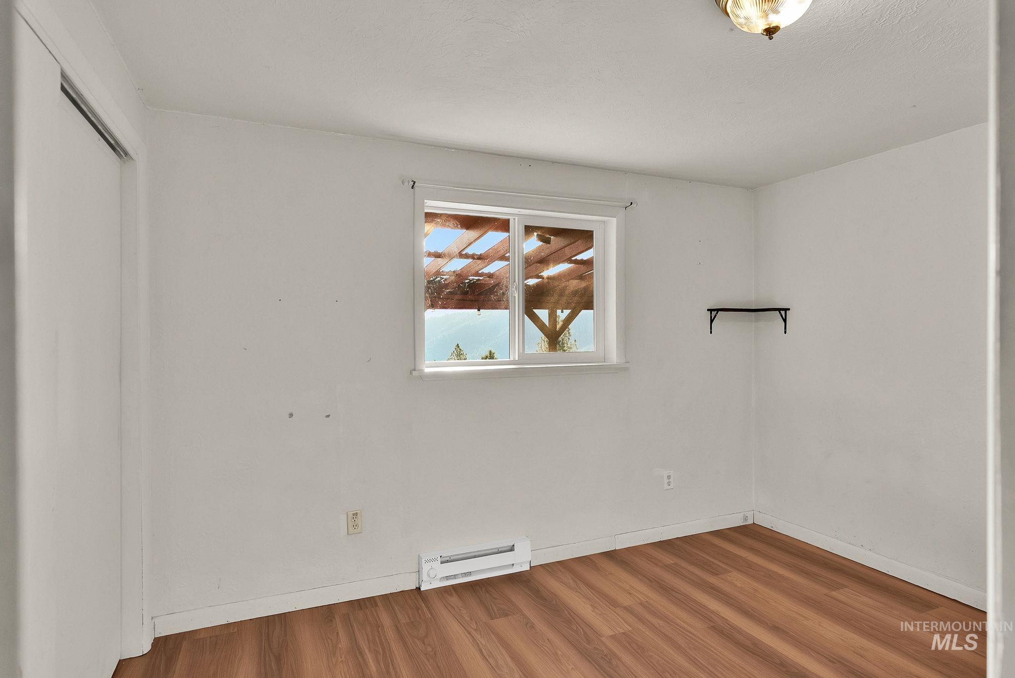 Unfurnished room with wood finished floors and a baseboard radiator