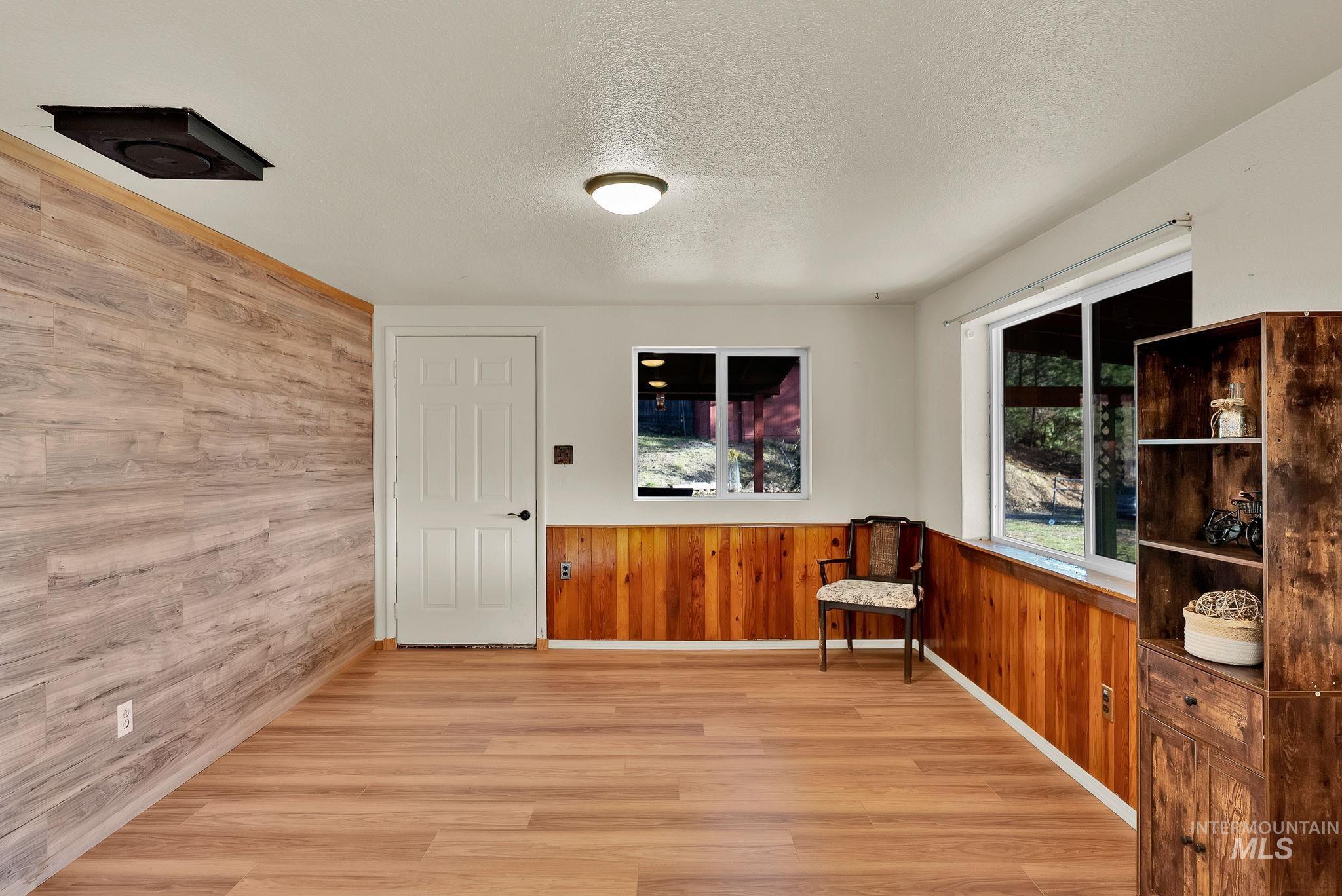 Unfurnished room featuring wooden walls, light wood-style floors, a textured ceiling, and a wainscoted wall