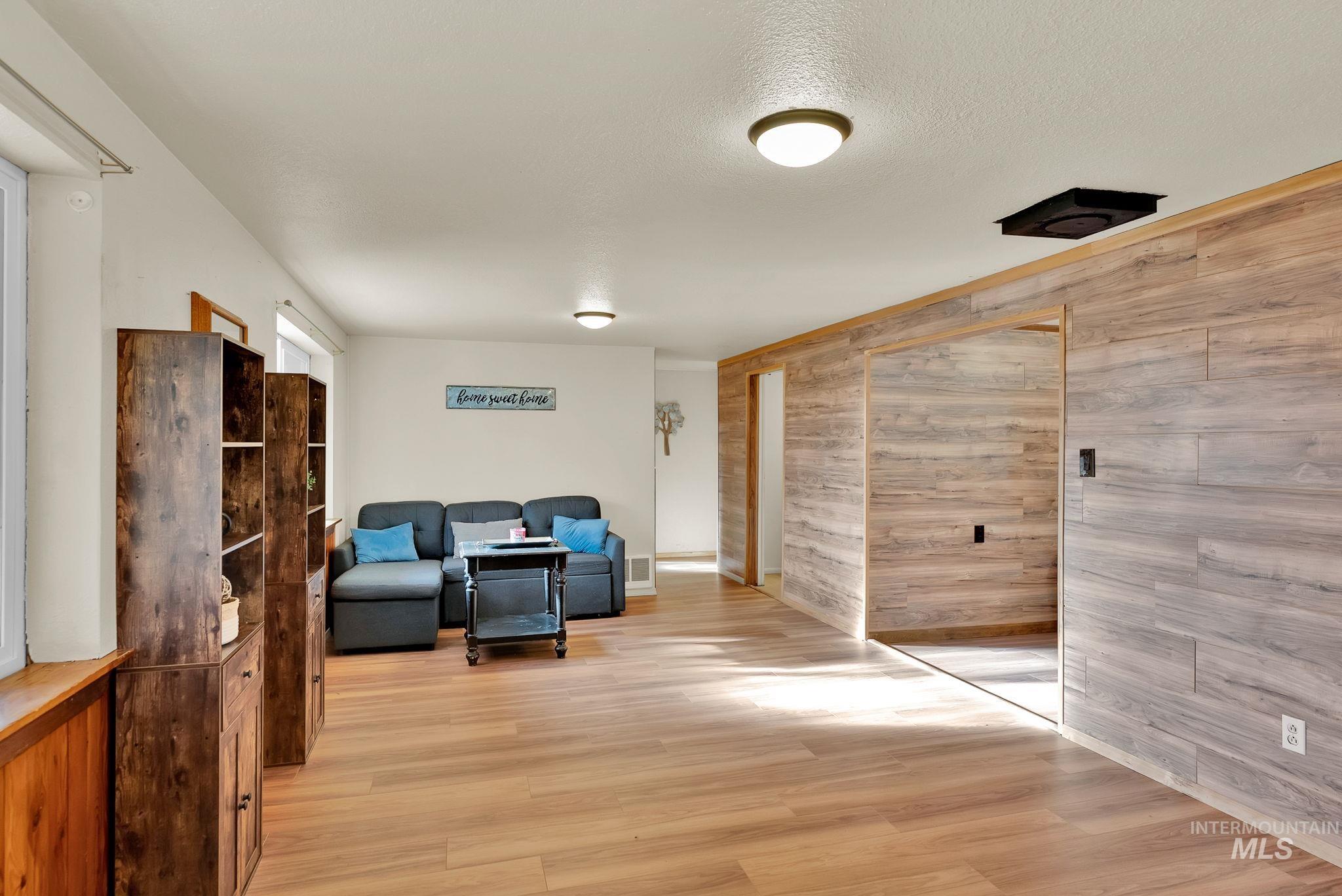 Living area with wooden walls, light wood-style floors, and a textured ceiling
