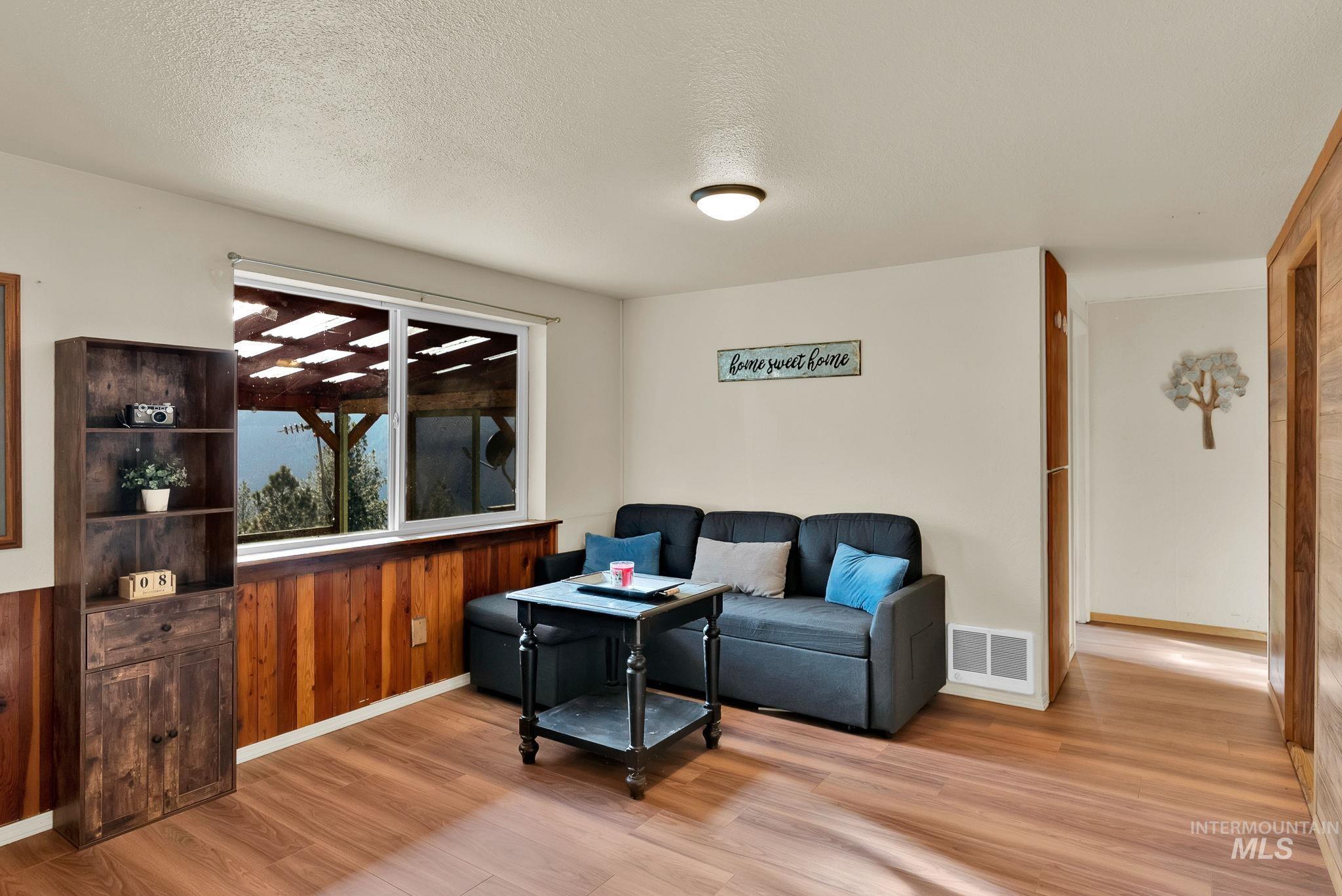Living room with light wood-style floors, wooden walls, and a textured ceiling